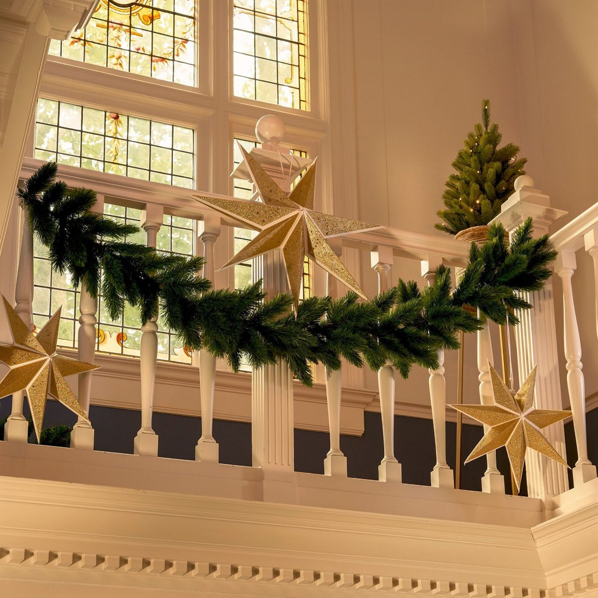 Un garde-corps d'escalier blanc décoré d'une guirlande de pin verte, de trois étoiles dorées et d'un sapin.