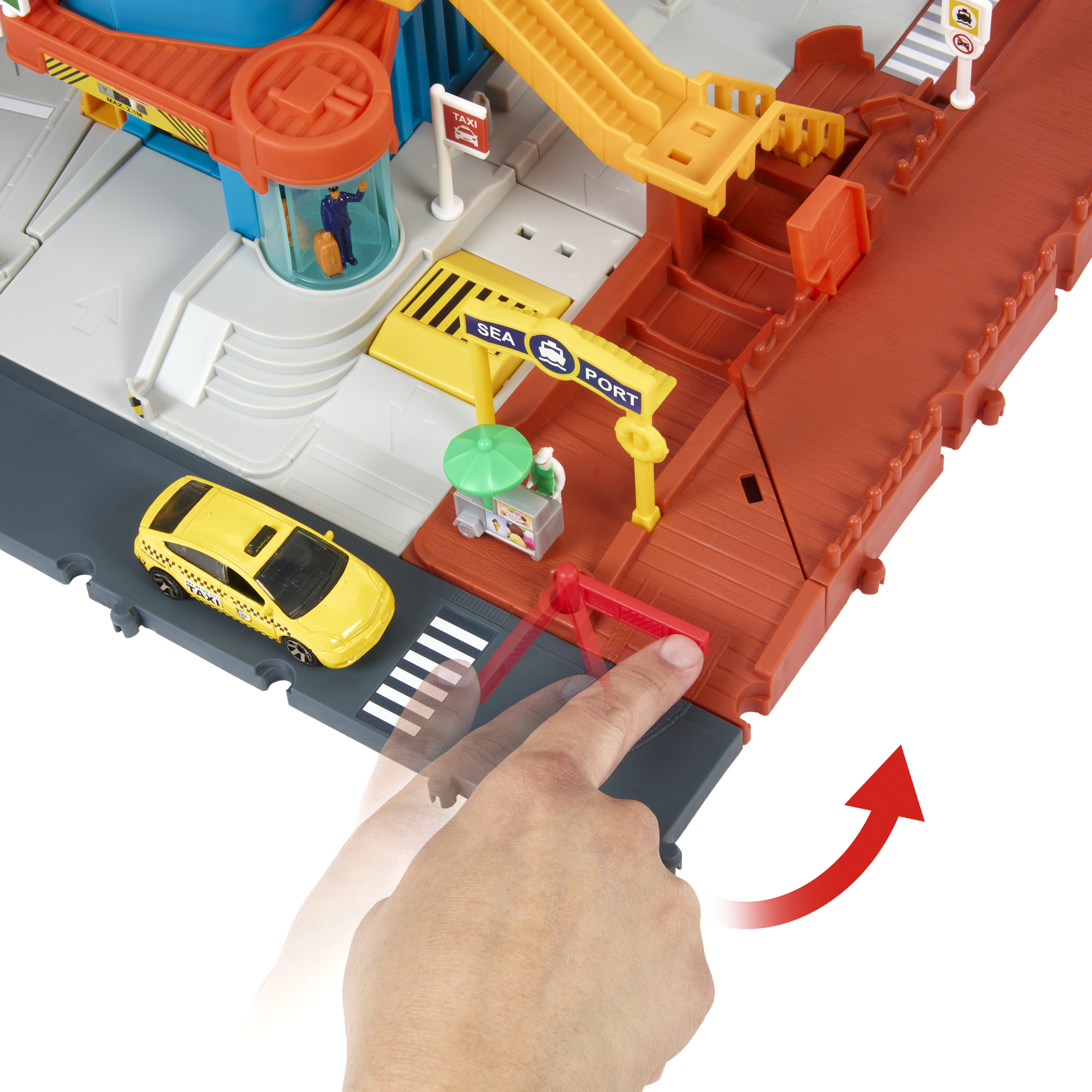 Hand berührt eine rote Schranke an einem bunten Spielplatz mit gelbem Taxi und Hafen.