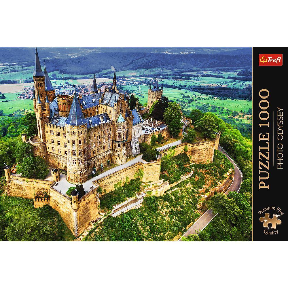 Luftaufnahme der Burg Hohenzollern auf einem Hügel, umgeben von grünen Wäldern, mit einer Straße unten.