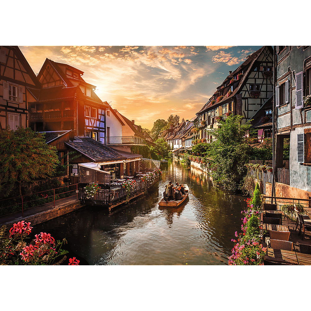 Ein Boot mit Menschen fährt im Sonnenuntergang auf einem von Fachwerkhäusern gesäumten Kanal.