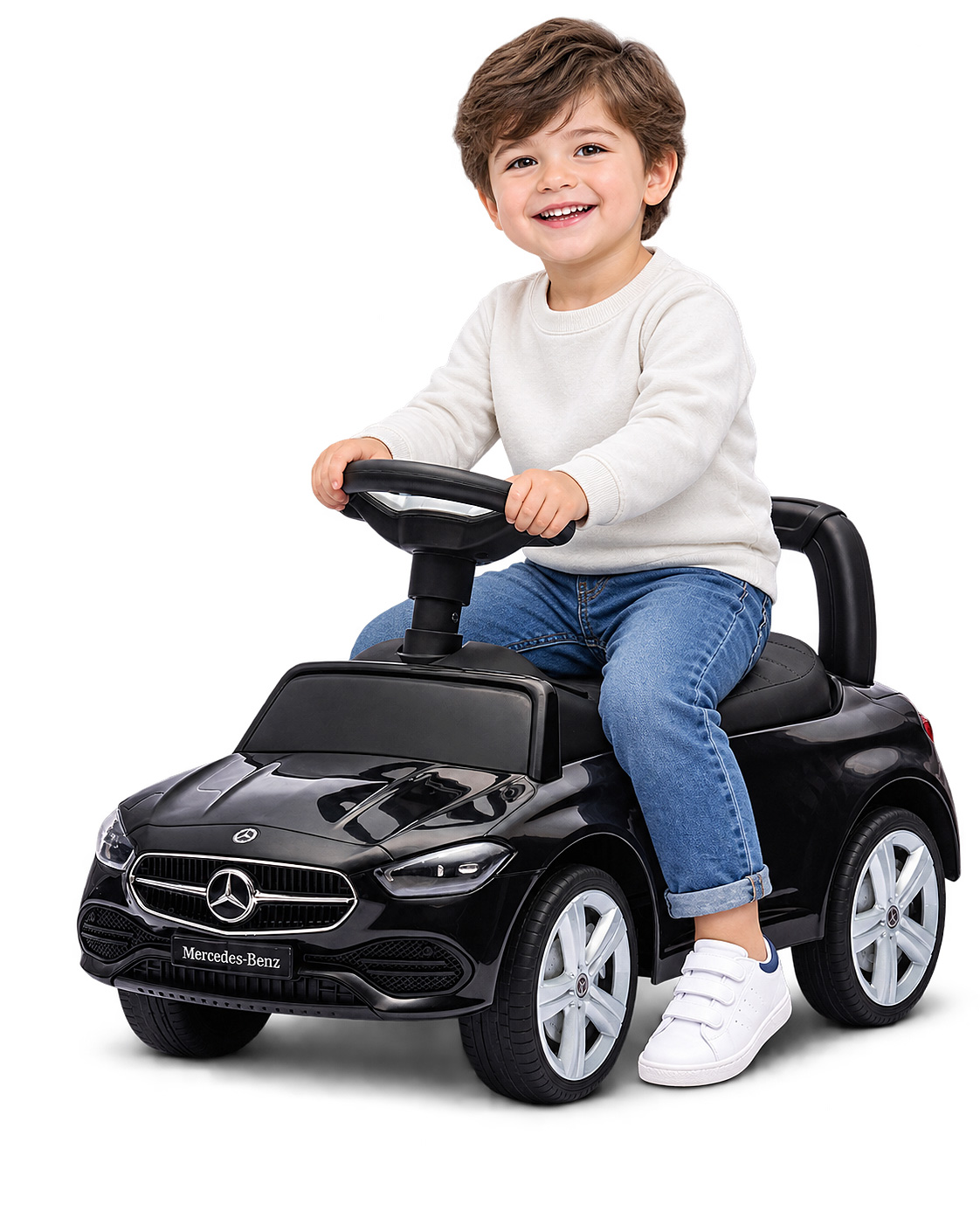 Kleiner Junge im weißen Pullover und blauen Jeans sitzt lächelnd auf einem schwarzen Mercedes-Benz Rutschauto.