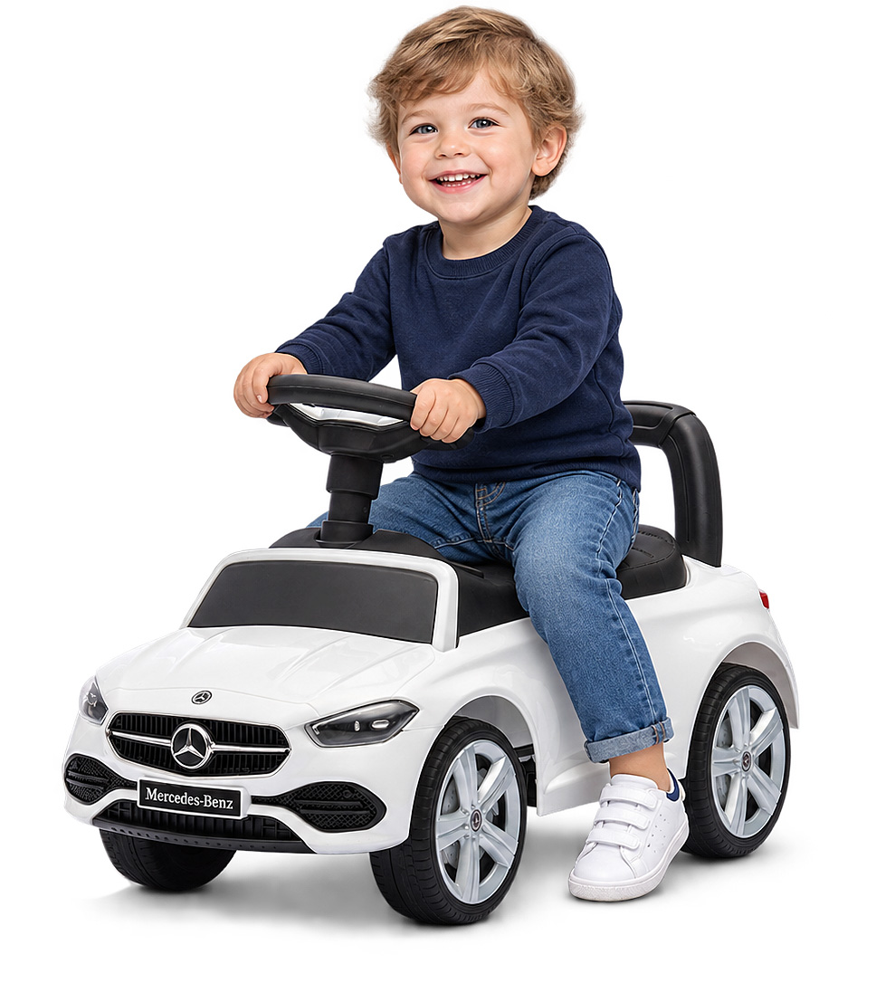 Ein glücklicher Junge sitzt auf einem weißen Mercedes-Benz Spielzeugauto vor weißem Hintergrund.