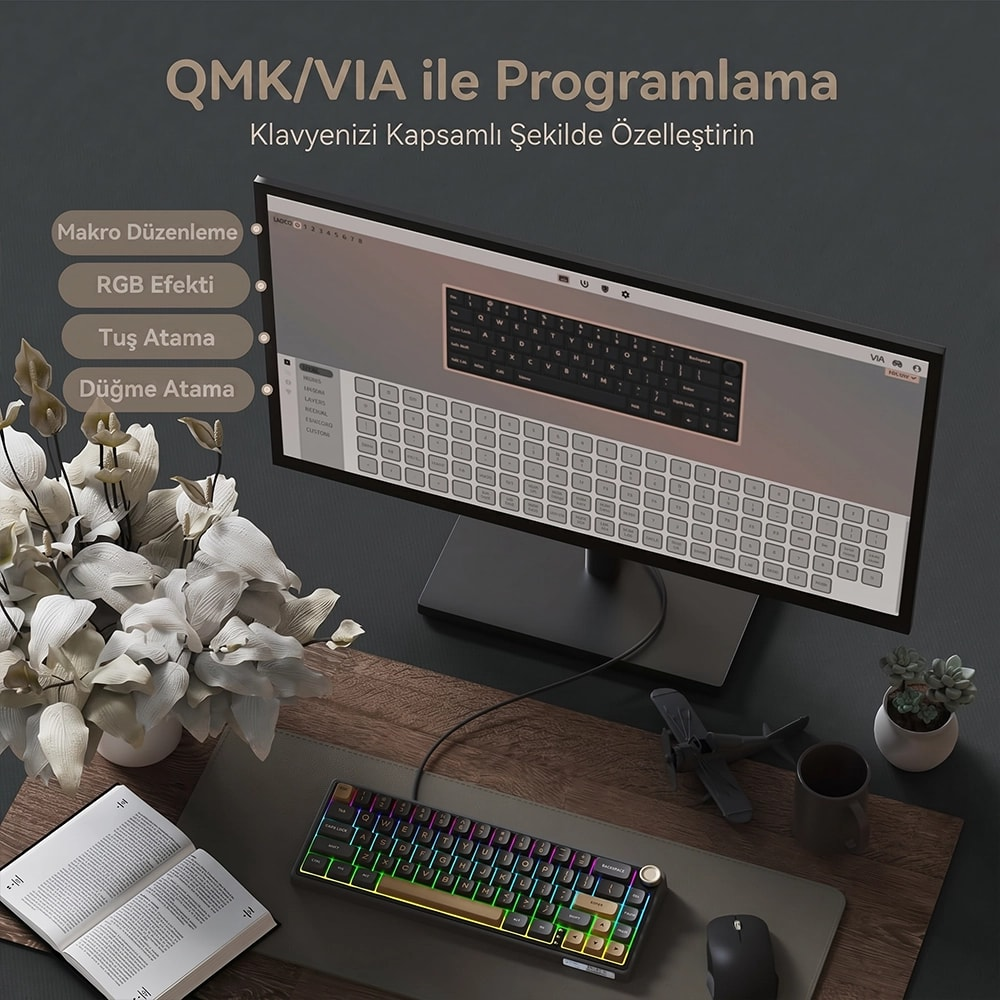 Monitör, RGB mekanik klavye, açık kitap ve dekoratif bitkiler içeren bir masa düzeni.