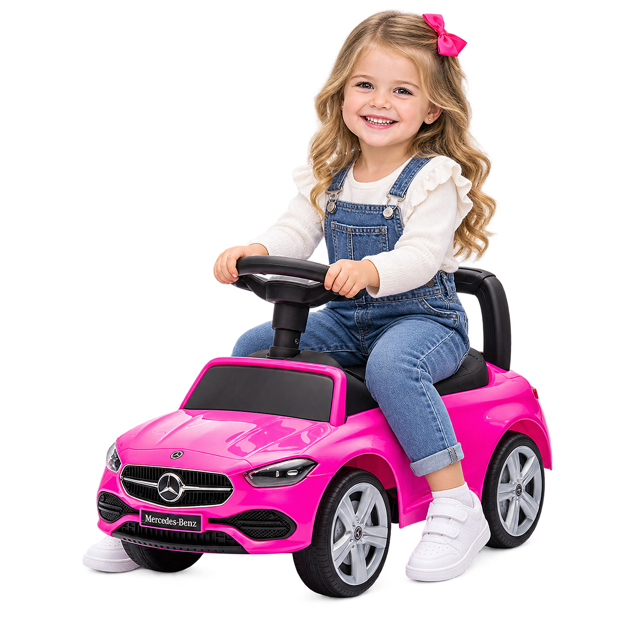 Ein smiling Mädchen sitzt in einem rosa Mercedes-Benz Spielzeugauto auf weißem Hintergrund.