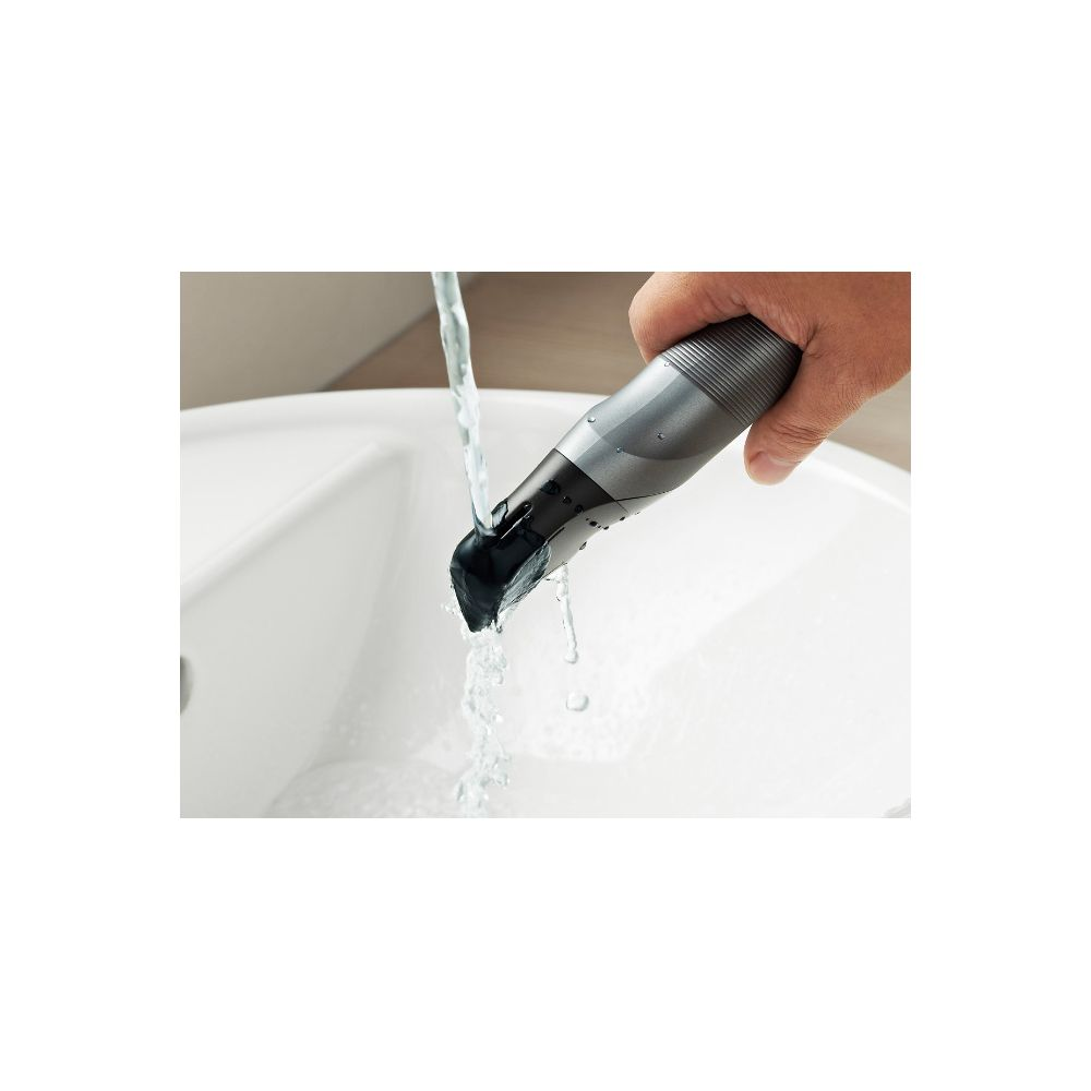 Un tagliacapelli portatile viene sciacquato sotto l'acqua corrente sopra un lavandino bianco.