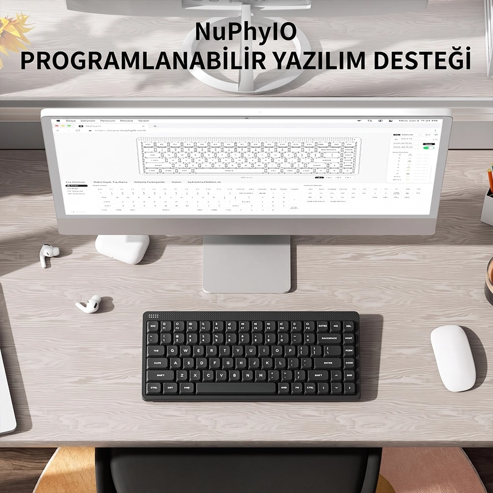 Drewniane biurko z monitorem, czarną klawiaturą, białą myszką i słuchawkami bezprzewodowymi.