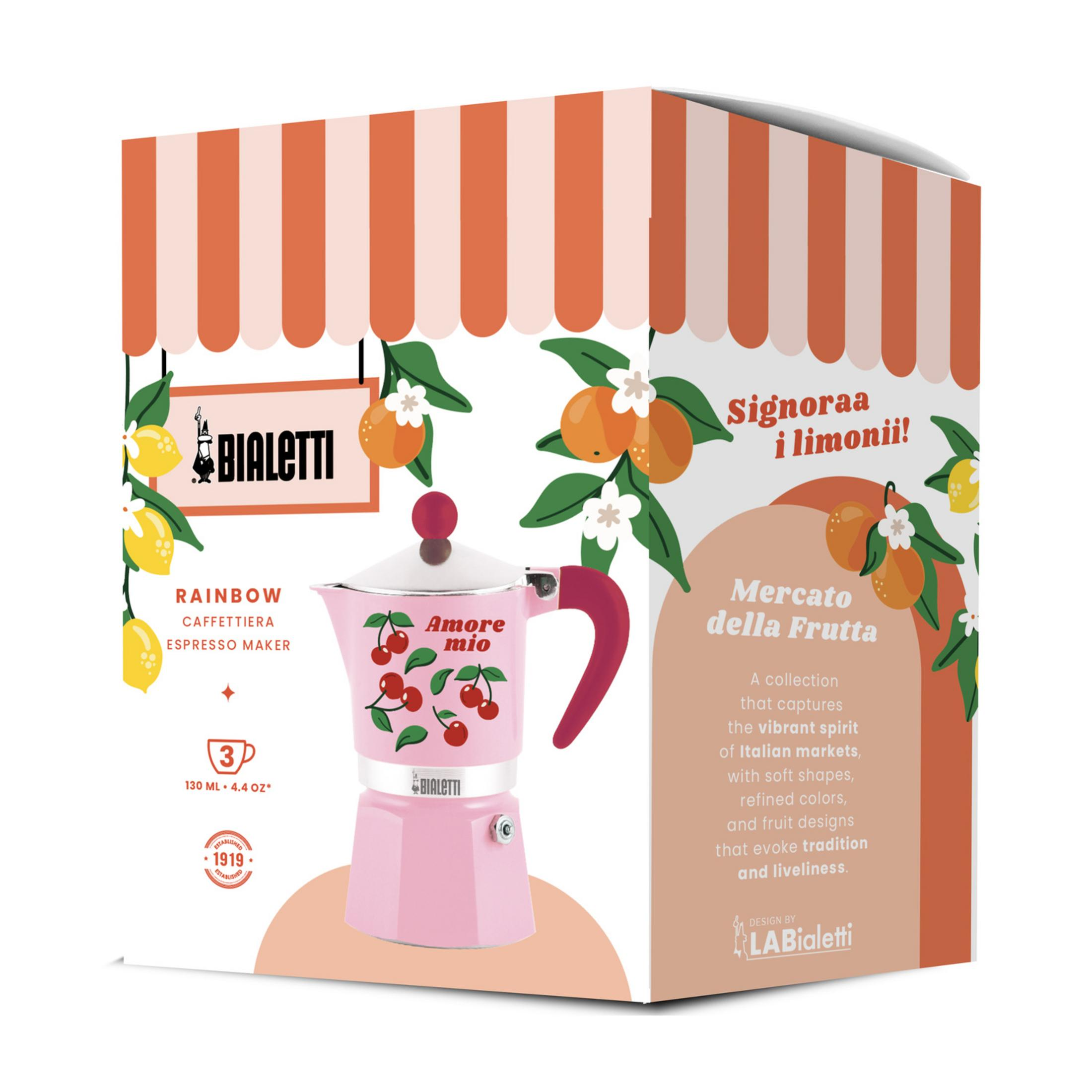 Una moka Bialetti rosa con ciliegie su una scatola illustrata con arance e limoni.