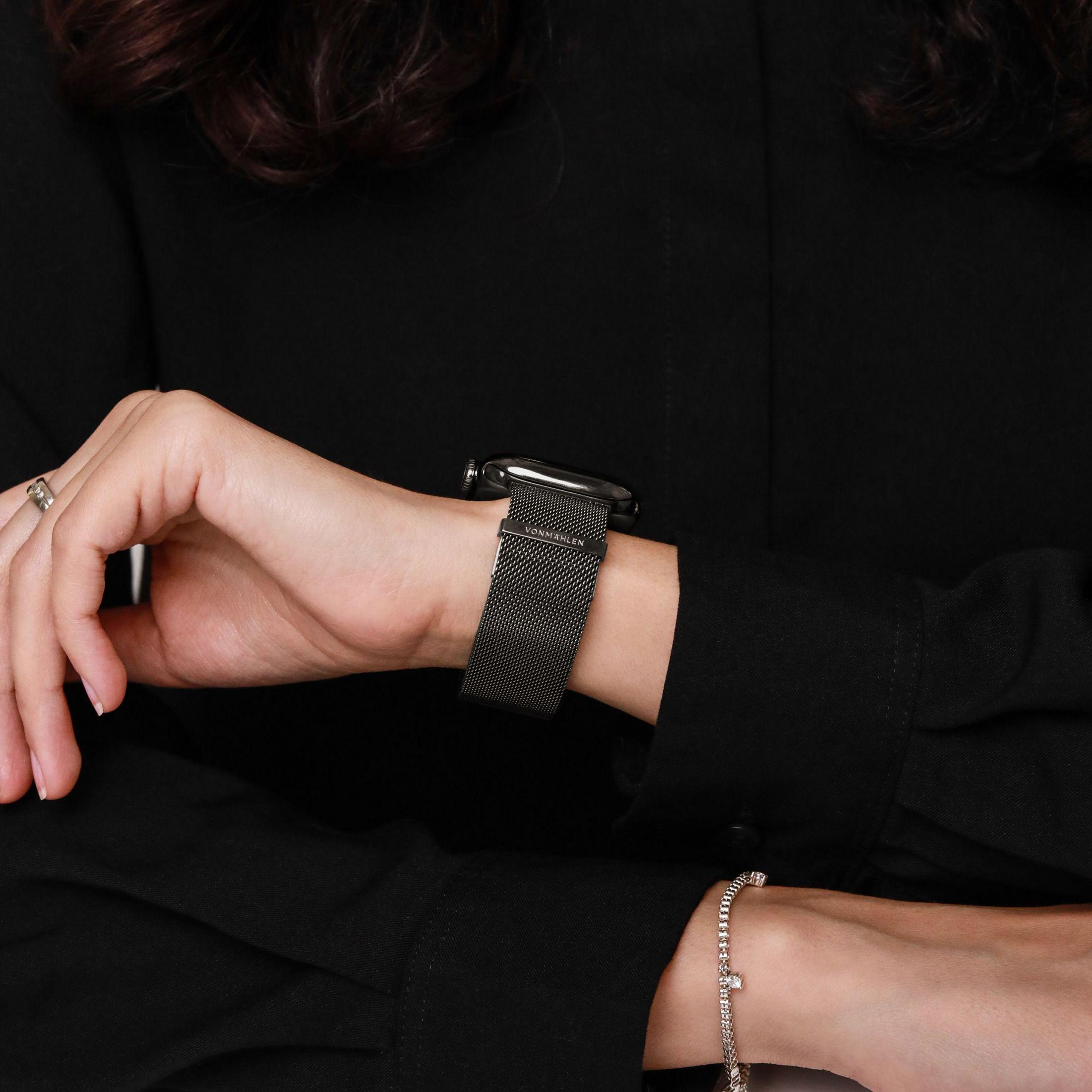 Persona in abito nero indossa uno smartwatch nero con cinturino in maglia di metallo.