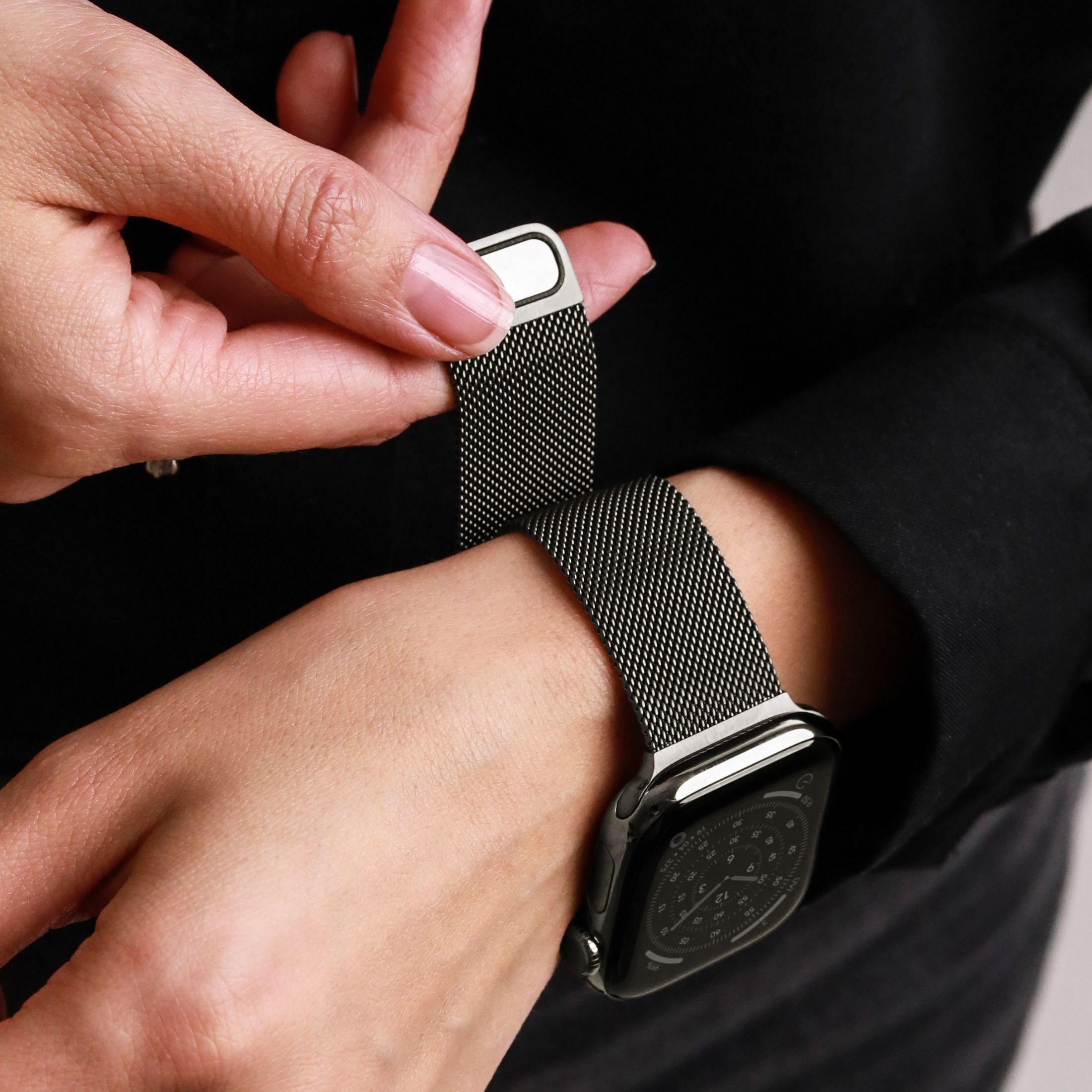 Persona che regola un cinturino in maglia milanese scura su uno smartwatch.