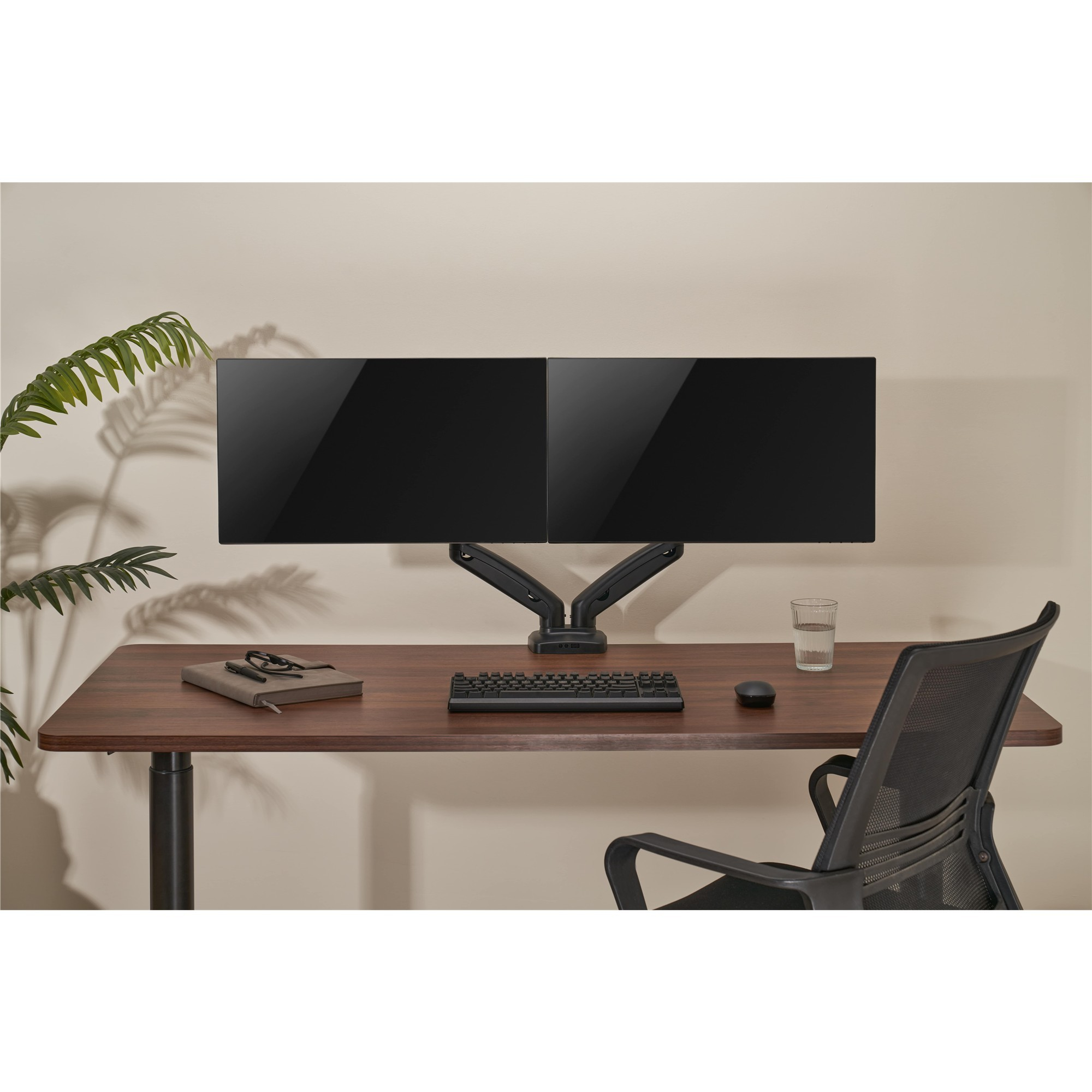 Ein hölzerner Schreibtisch mit zwei Monitoren, Tastatur, Maus, Notizbuch und einer Pflanze daneben.
