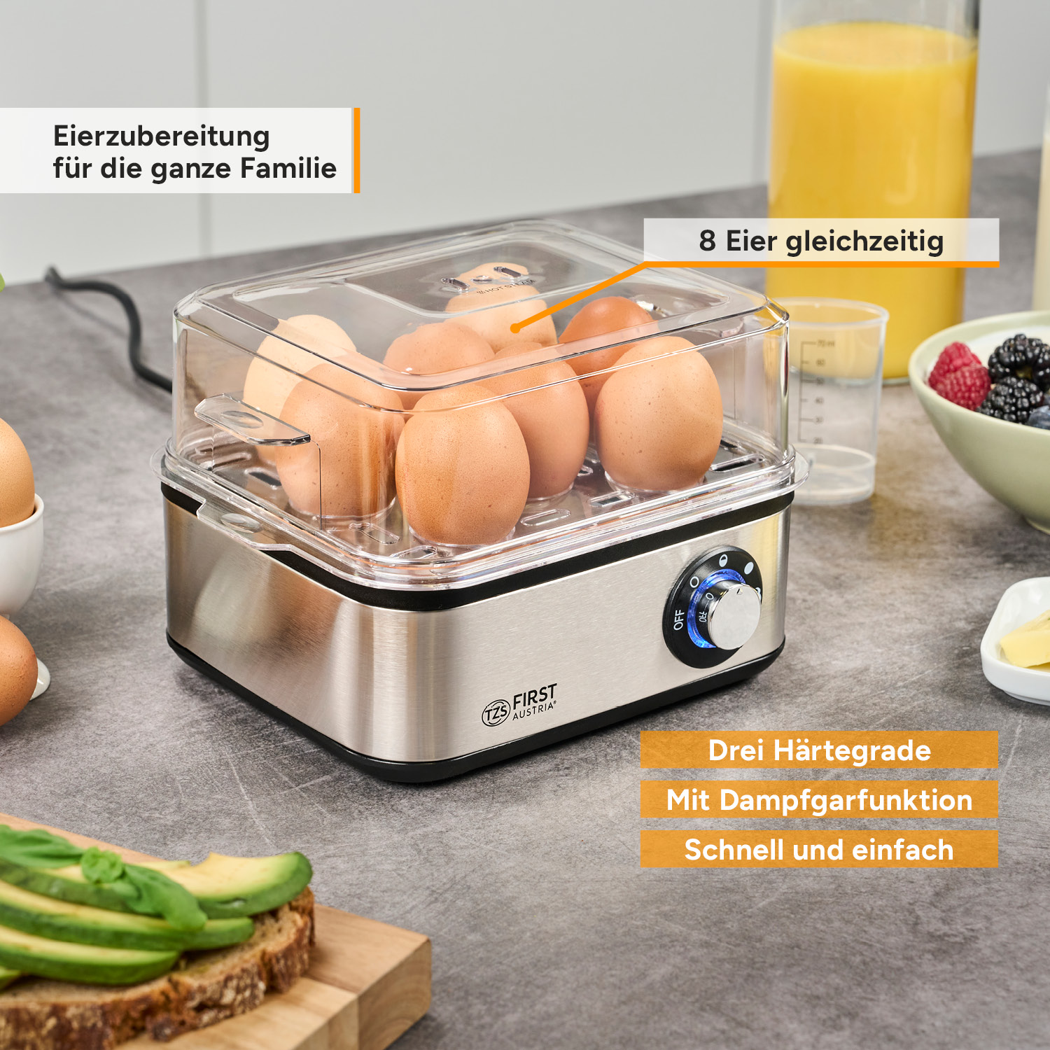 Ein Eierkocher aus Edelstahlt mit Eiern darin steht auf einer grauen Küchentheke mit Frühstückszutaten.