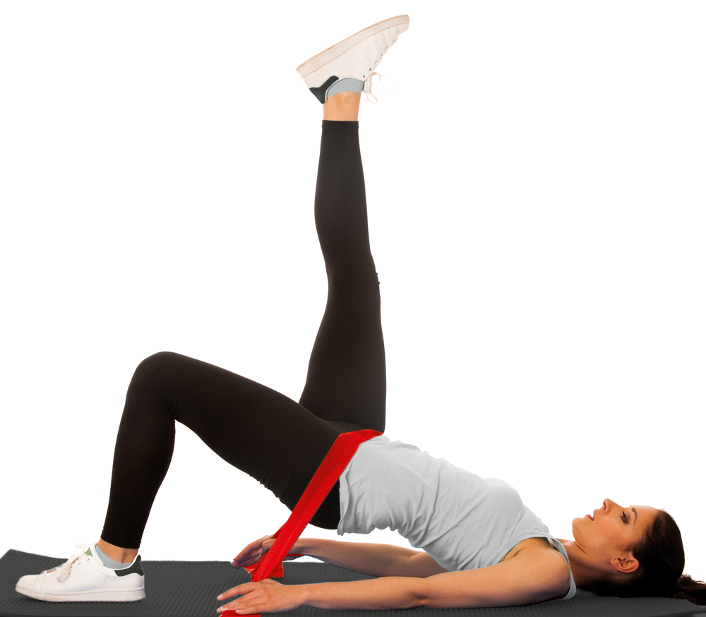 Eine Frau in Leggings liegt auf einer Matte und hebt ihr Bein, während sie ein Widerstandsband hält.