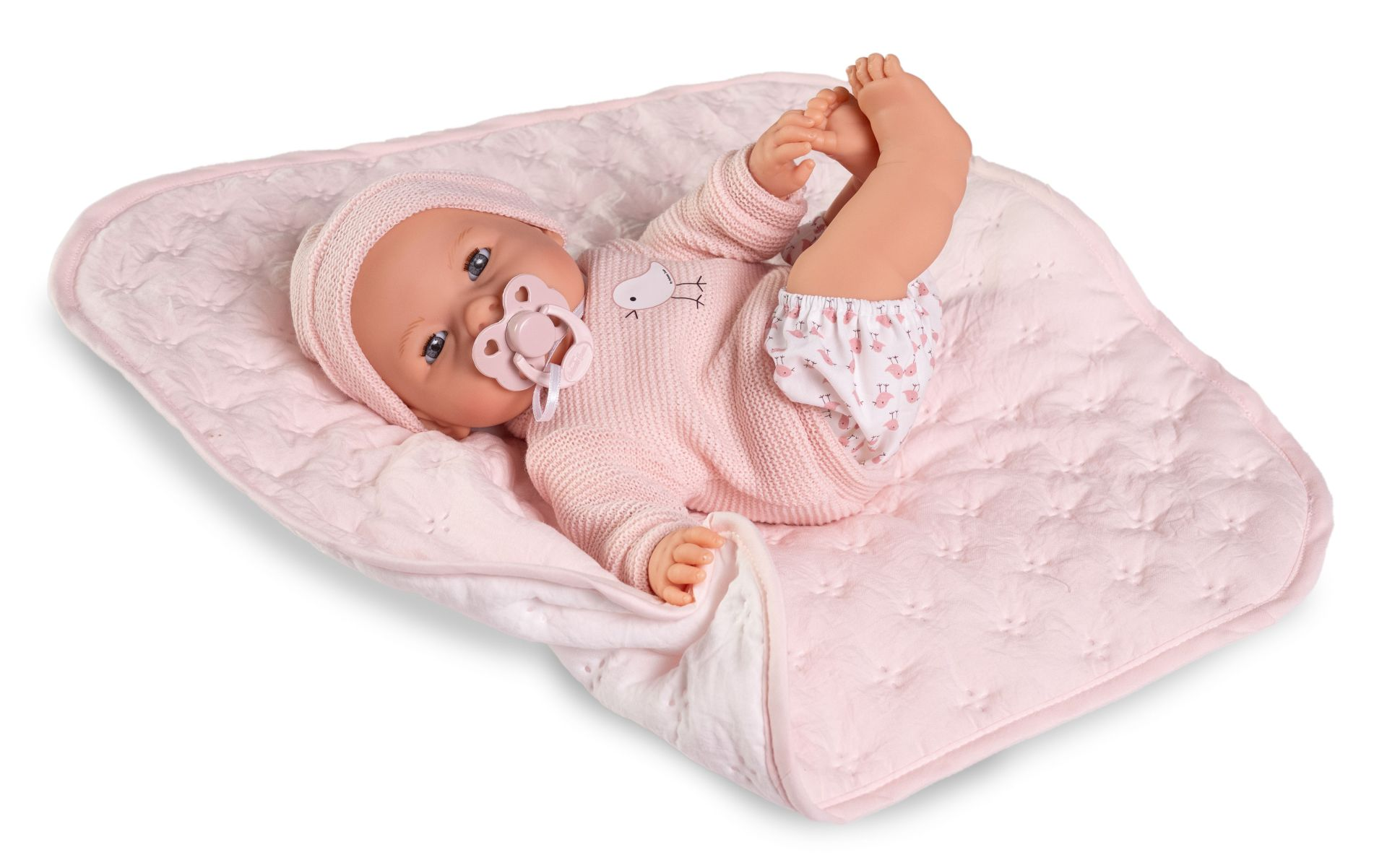 Un muñeco bebé con gorro de punto rosa y chupete yace sobre una manta rosa.