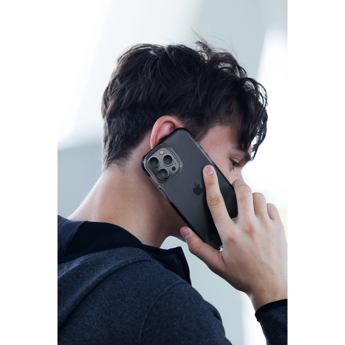 Koyu kapüşonlu bir adam kulağına siyah akıllı telefon tutuyor.