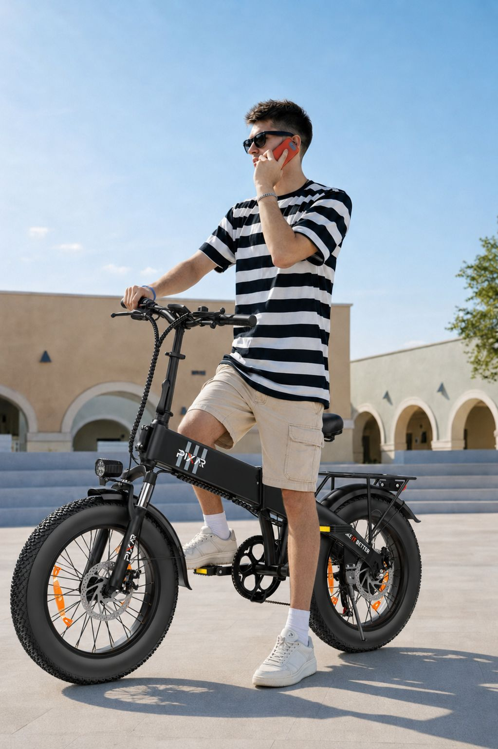 Un joven con una camisa de rayas blancas y negras habla por teléfono mientras está de pie en una bicicleta eléctrica.