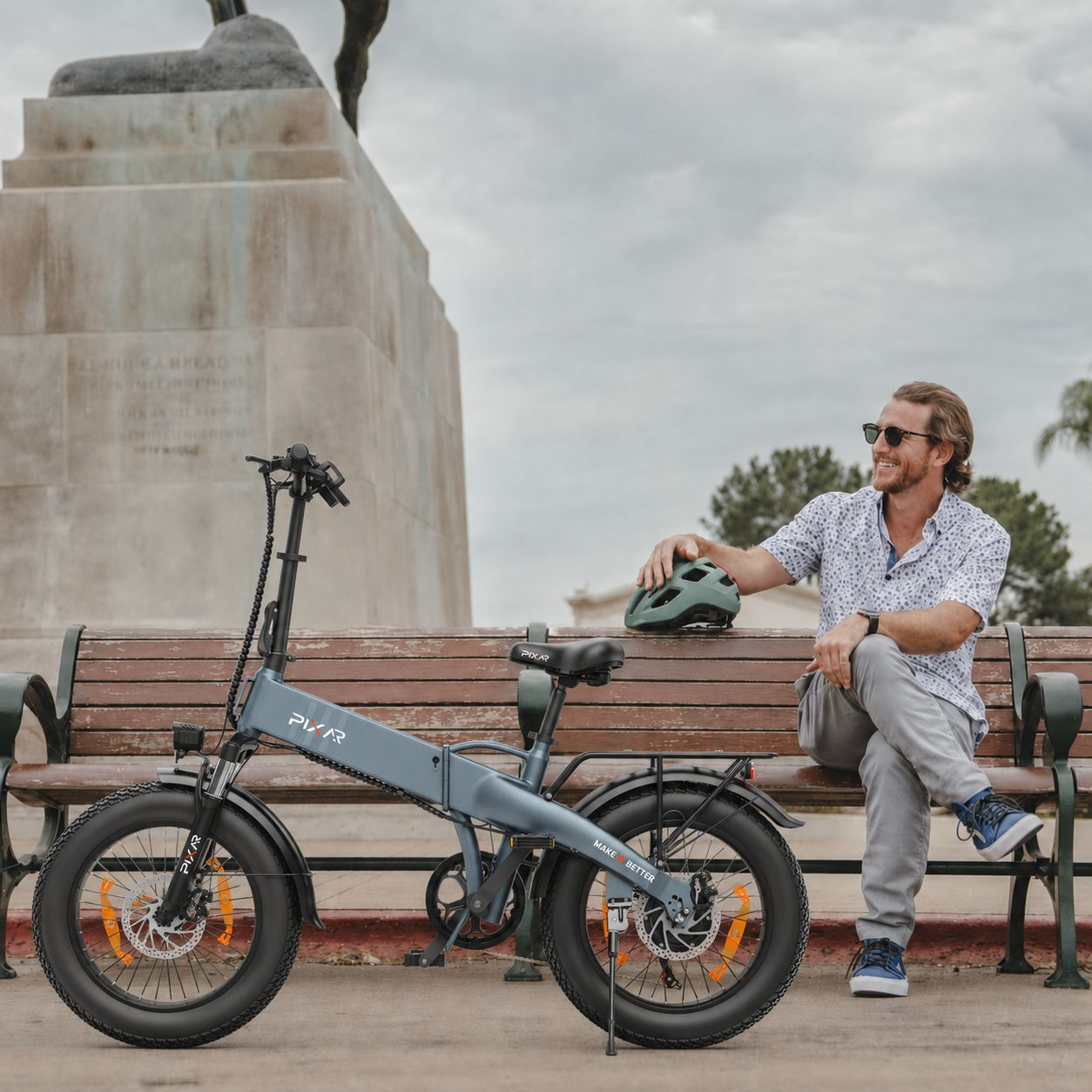 Un hombre sentado en un banco de parque junto a una bicicleta eléctrica azul.