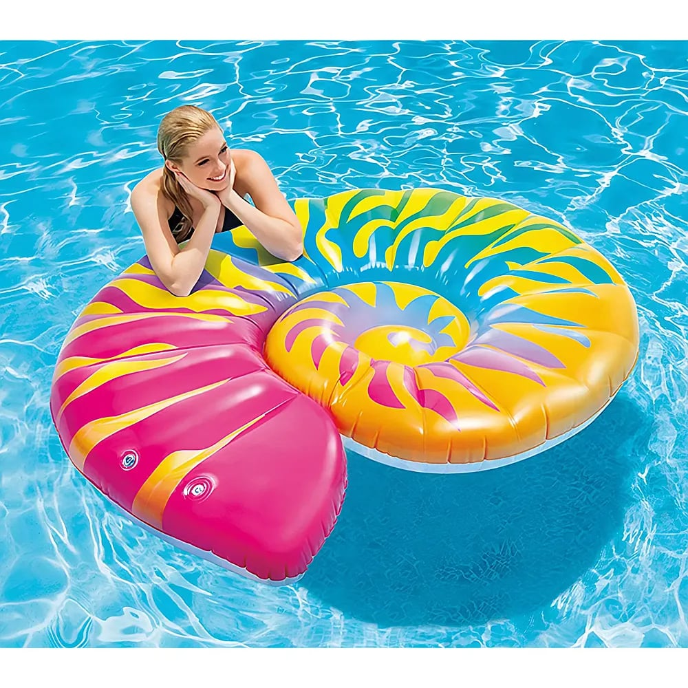 Una donna sorridente galleggia in una piscina su una grande e colorata zattera gonfiabile a forma di conchiglia.