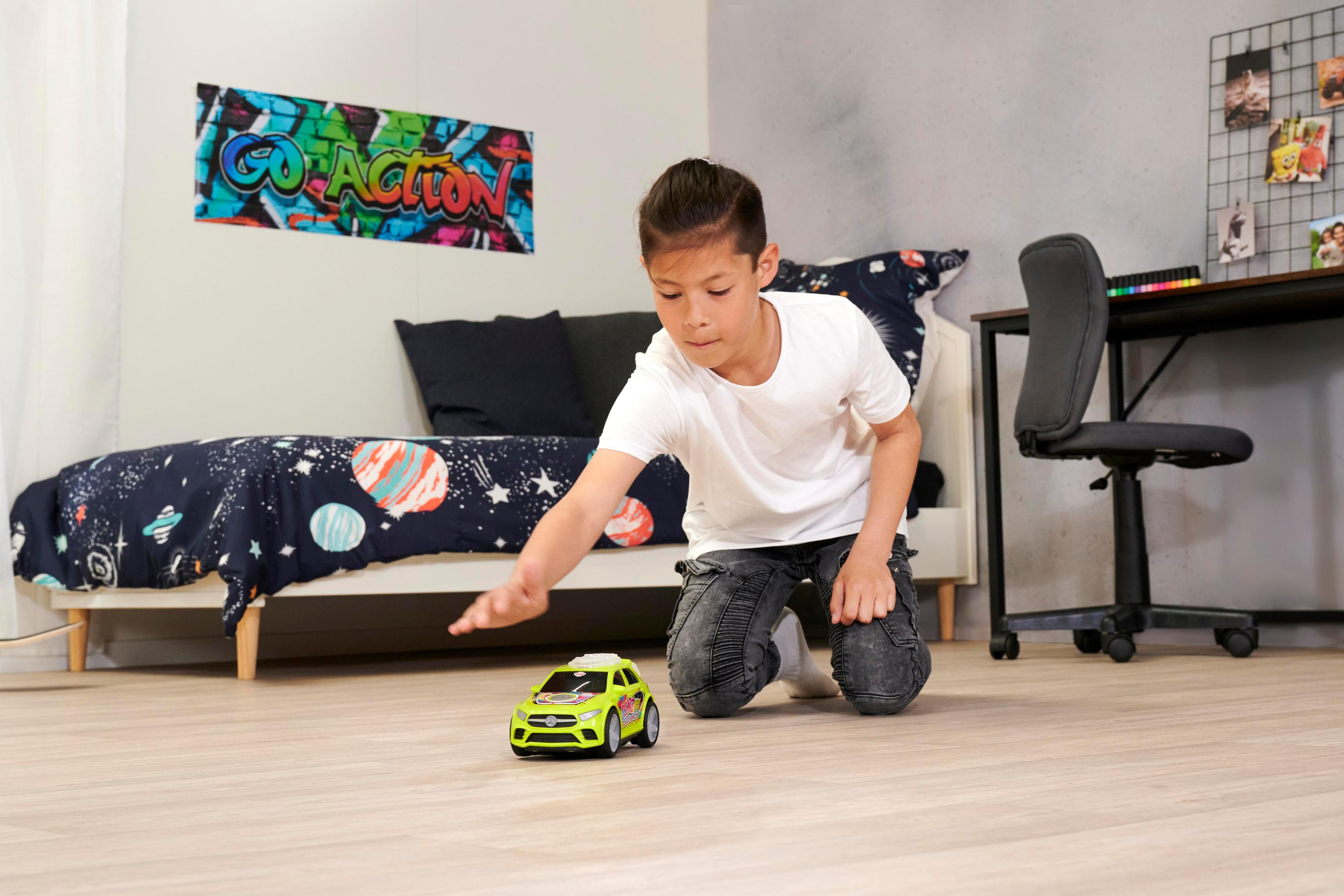 Ein Junge im weißen T-Shirt kniet auf dem Holzboden im Kinderzimmer und spielt mit einem kleinen grünen Spielzeugauto.