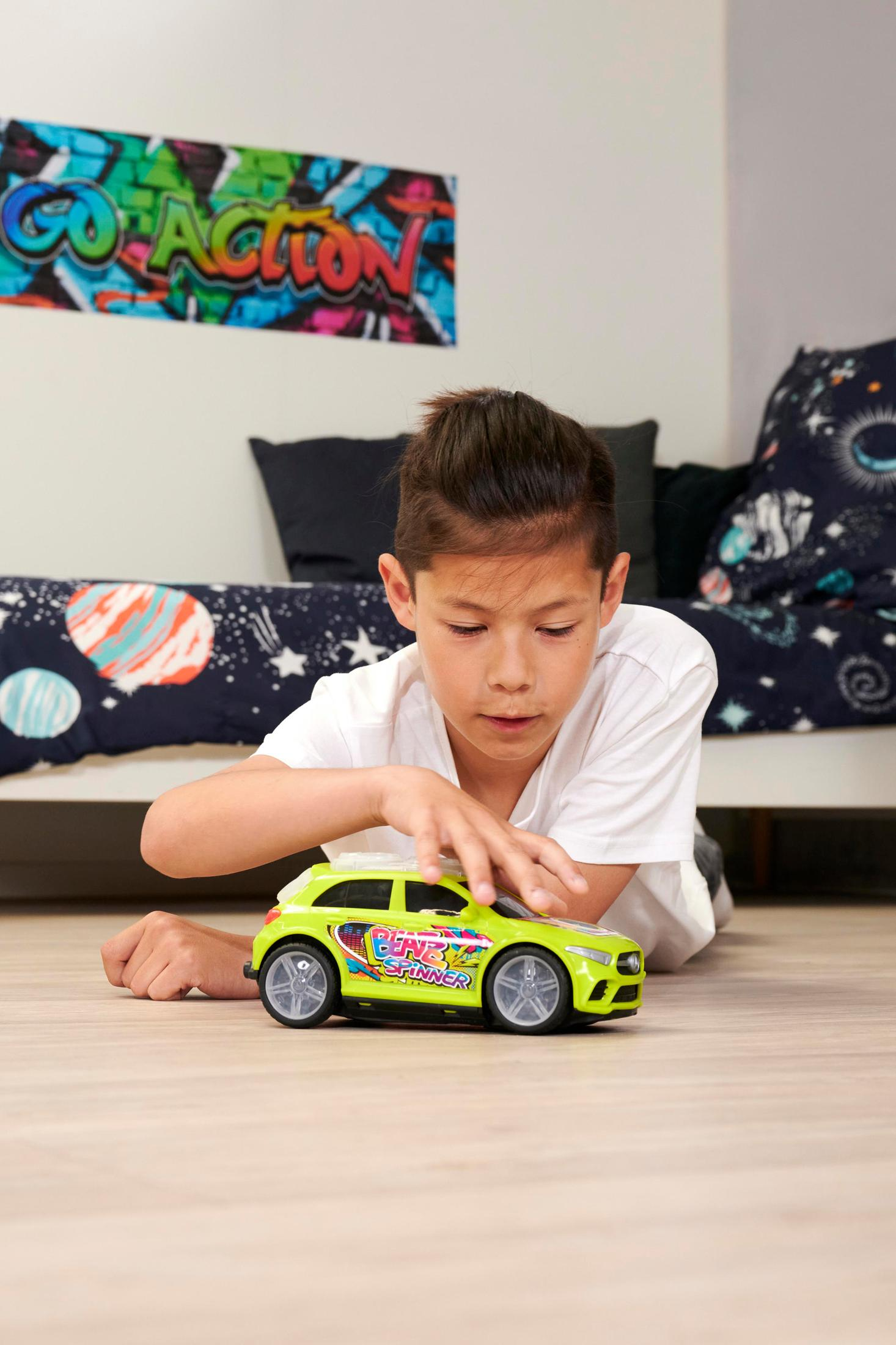 Ein Junge im T-Shirt liegt auf dem Holzboden und spielt mit einem grünen Spielzeugauto in einem Kinderzimmer.