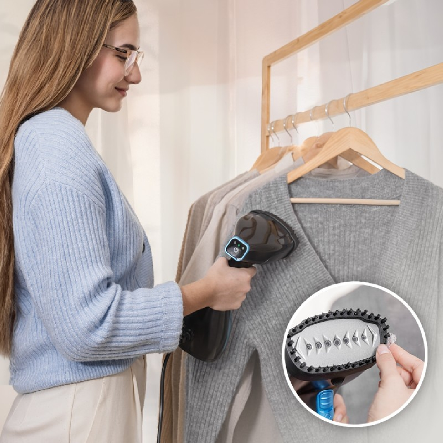 Una donna con un maglione blu usa un vaporizzatore su un maglione grigio appeso.