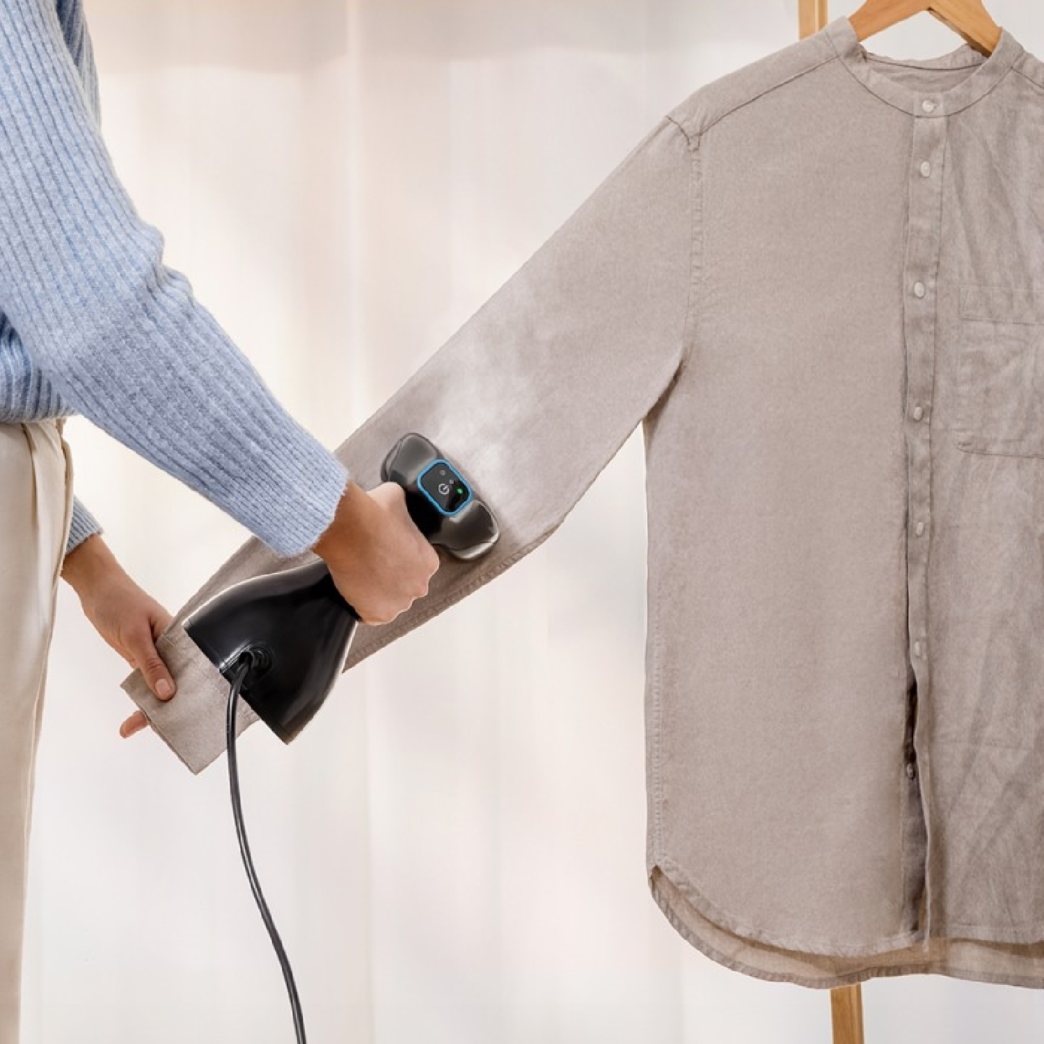 Una persona usa un vaporizzatore portatile nero su una camicia grigia appesa.