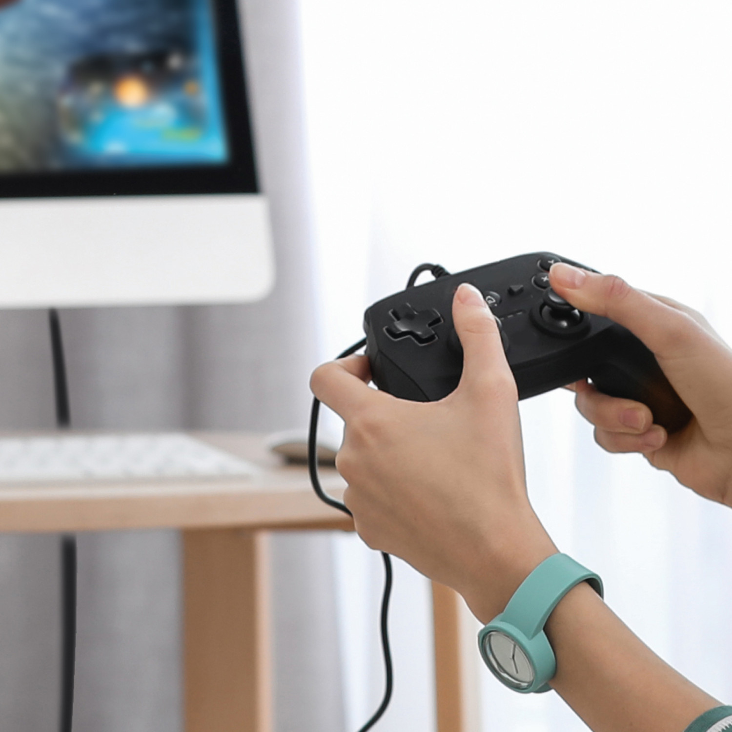 Una persona che indossa un orologio blu tiene un controller di gioco nero davanti a un computer.
