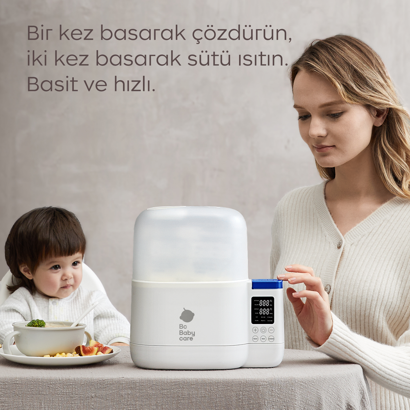 Bir kadın, bebeğin yanında elektrikli biberon ısıtıcısını kullanıyor, Türkçe yazı var.