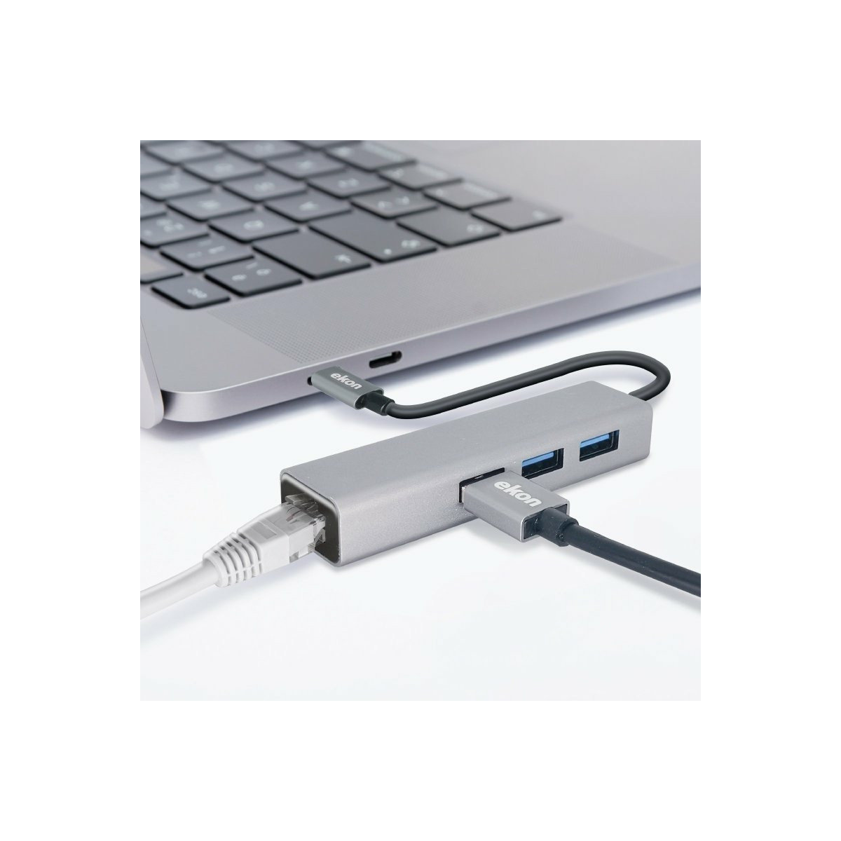 Un concentrateur USB-C gris avec des câbles connectés et un câble Ethernet à côté du clavier d'un ordinateur sur fond blanc.