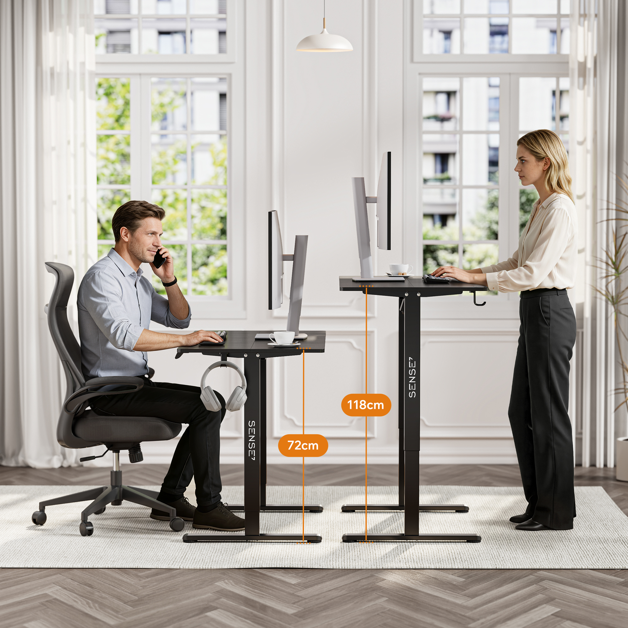 A man sits at a low desk on a chair, while a woman stands at a taller desk, both working in an office.