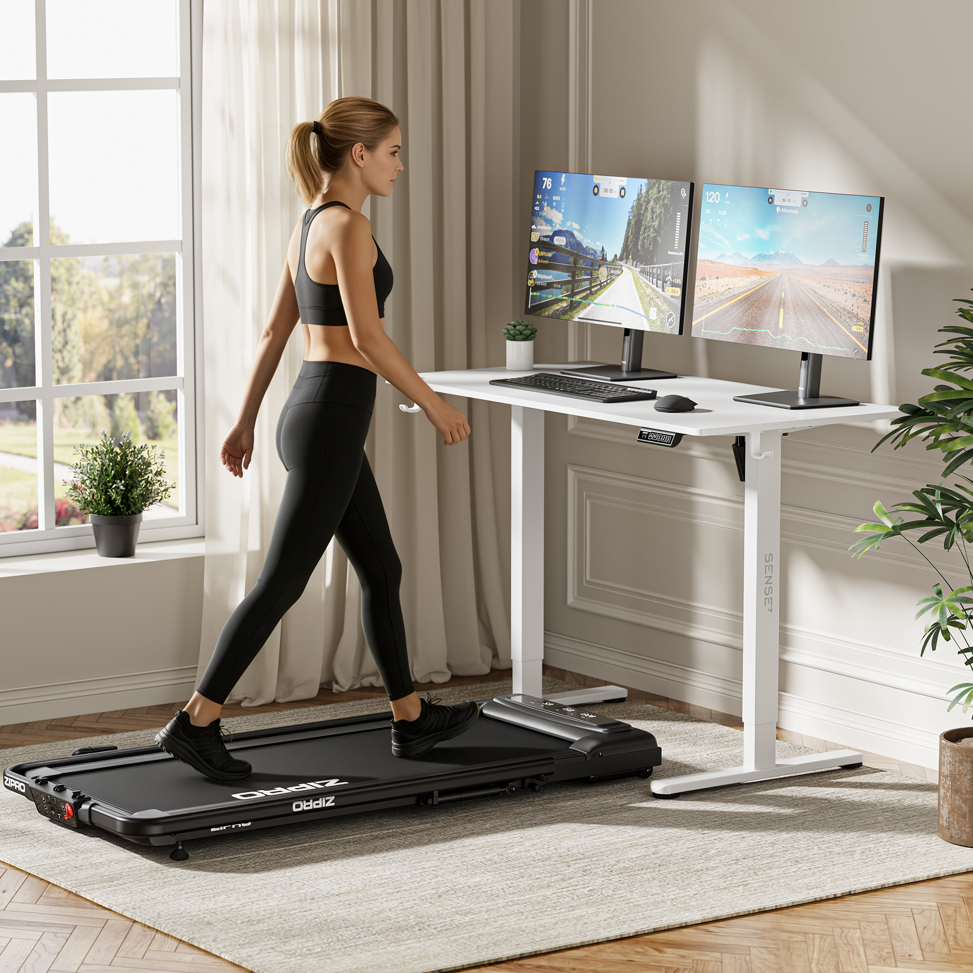 A woman walks on a treadmill at a white standing desk with dual monitors in a bright, modern room.