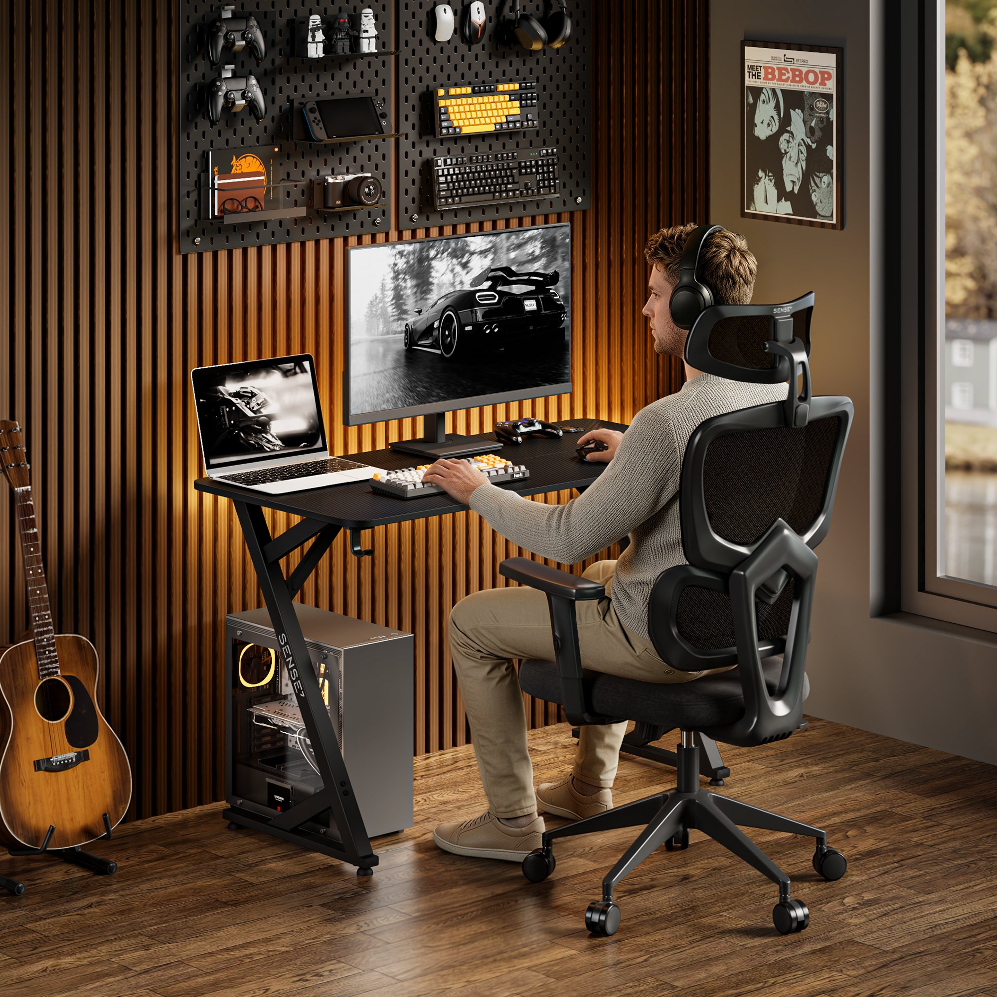 Ein Mann sitzt in einem Gaming-Stuhl und nutzt einen PC und Laptop vor einer holzvertäfelten Wand.