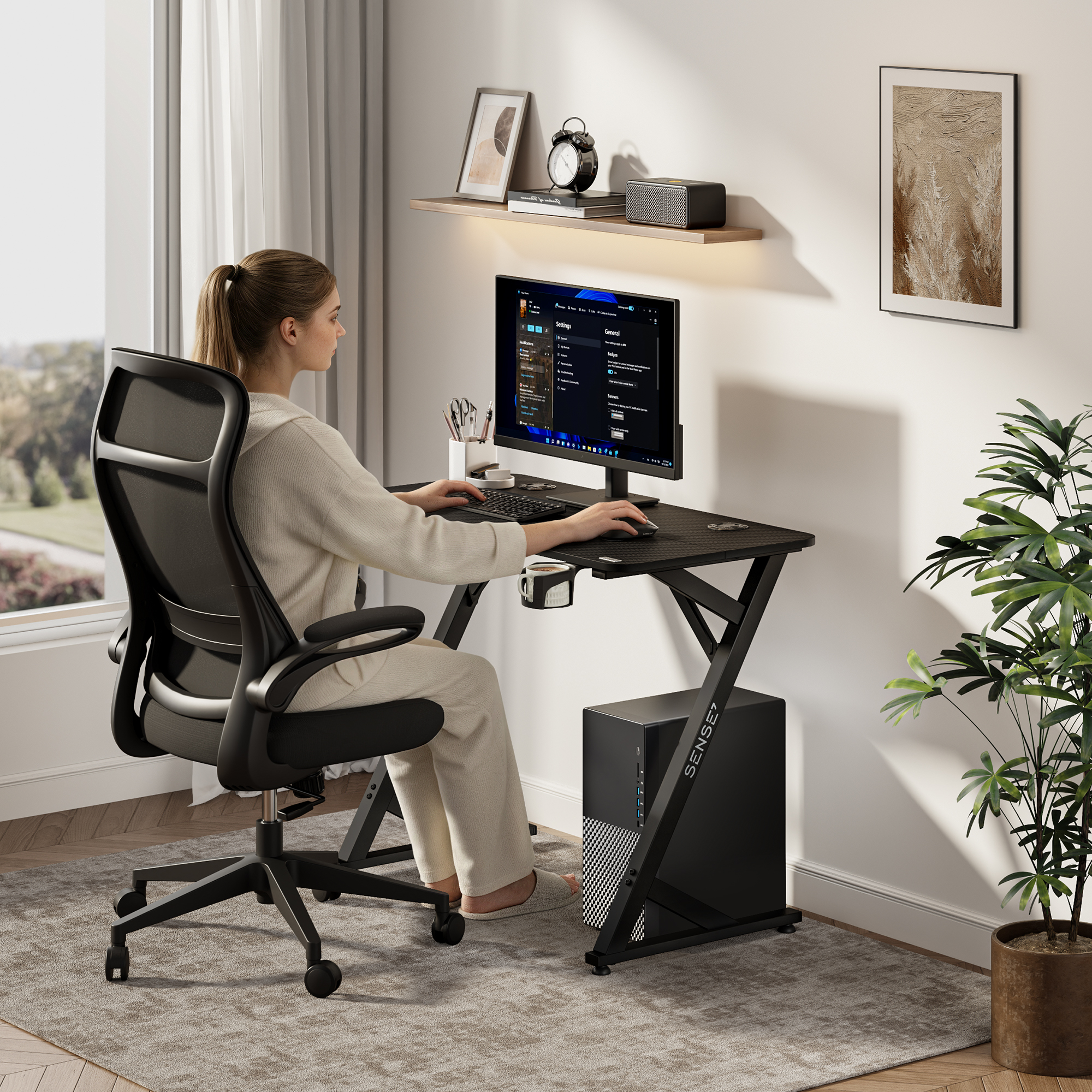 A woman sits at a black desk, typing on a keyboard and looking at a computer monitor.