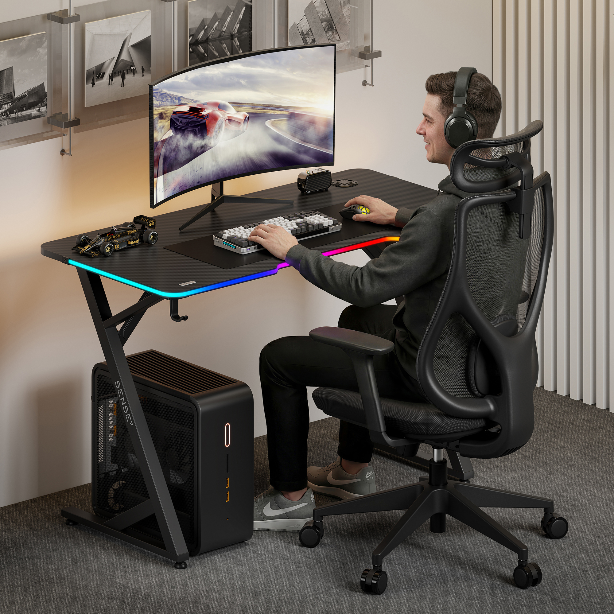 Ein junger Mann sitzt an einem schwarzen Gaming-Schreibtisch mit RGB-Beleuchtung, gebogenem Monitor und PC.