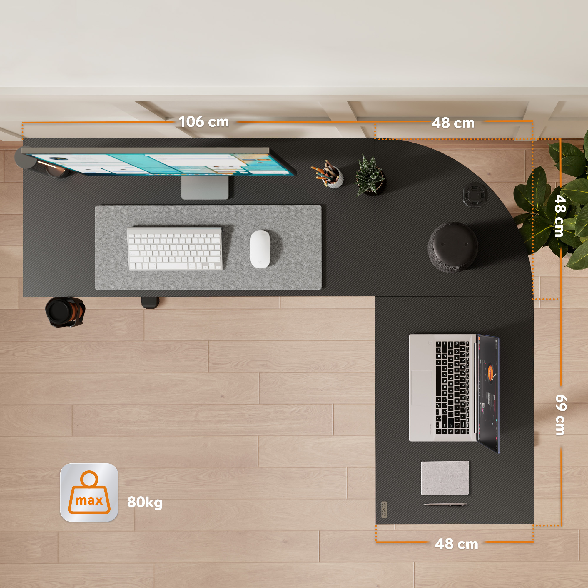 Top-down view of an L-shaped desk with a monitor, keyboard, laptop, and plants on a wooden floor.