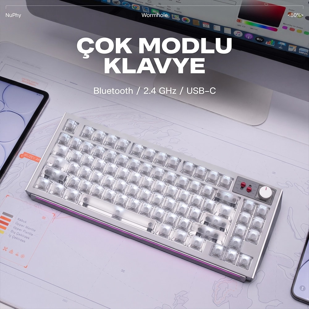 Przezroczysta klawiatura mechaniczna na biurku z tureckim tekstem i monitorem w tle.