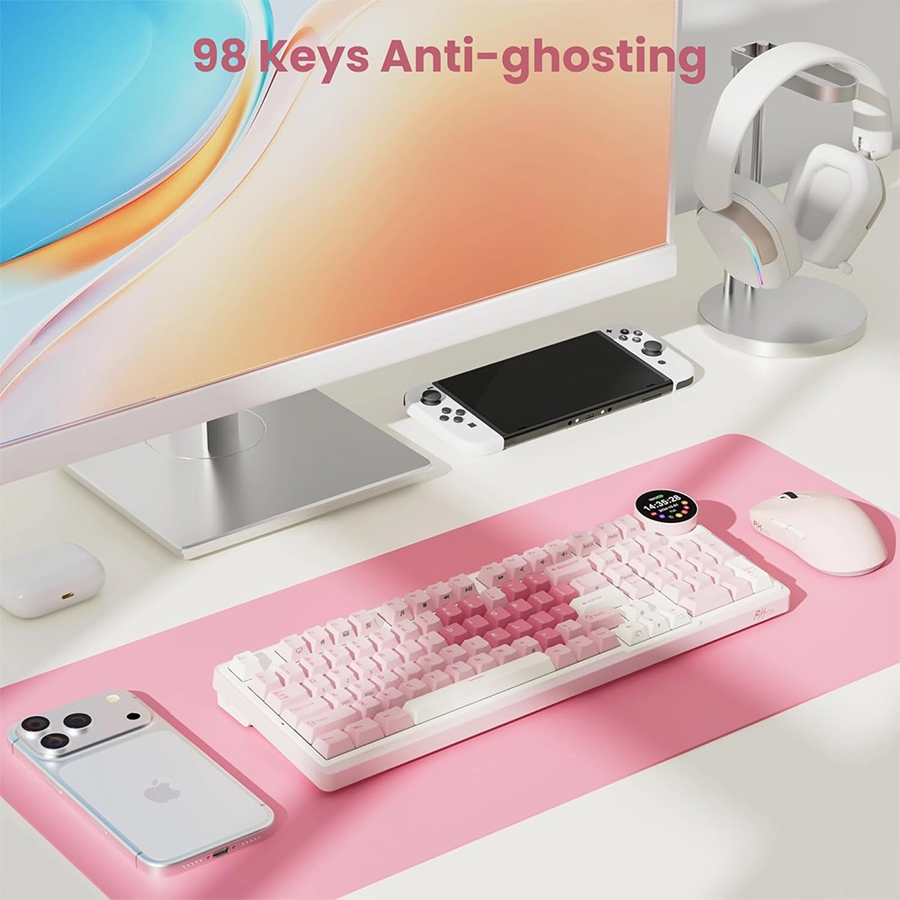 Monitör, pembe klavye, fare, akıllı telefon, el konsolu ve kulaklık bulunan bir masa düzeni.