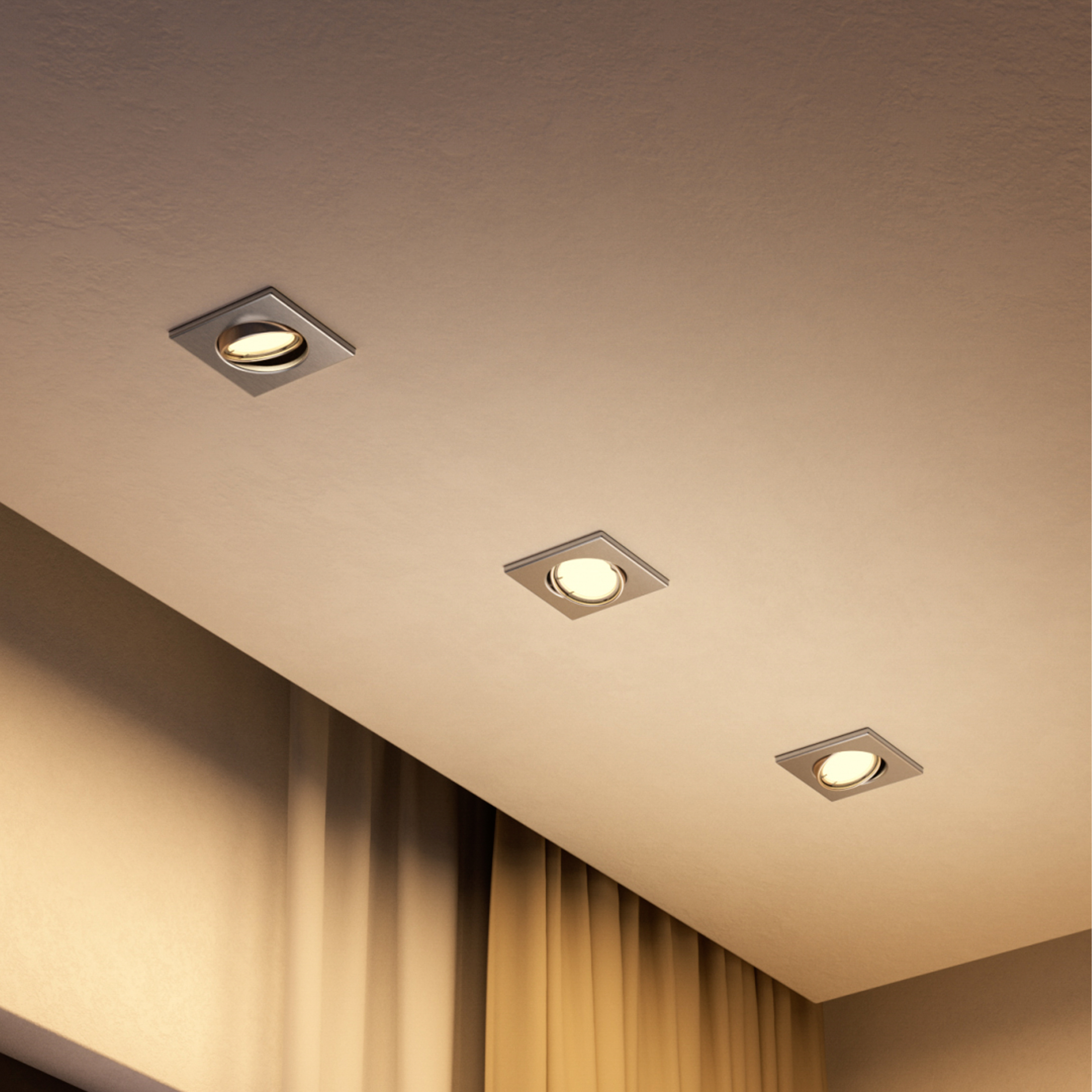 Tre faretti da incasso quadrati in un soffitto illuminato caldamente sopra tende dorate.