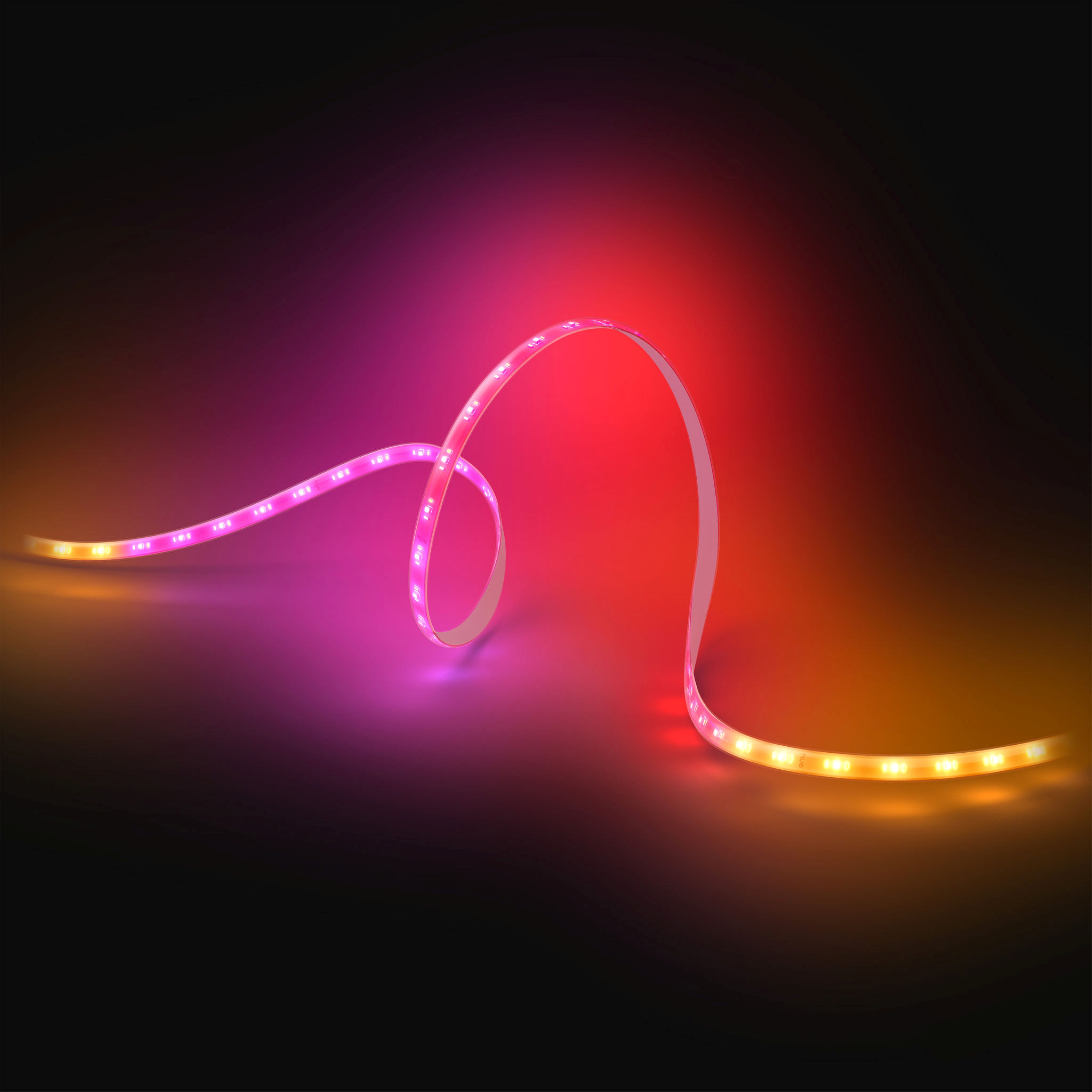 Una striscia LED flessibile si curva su sfondo scuro, emettendo luce rosa, rossa e arancione.
