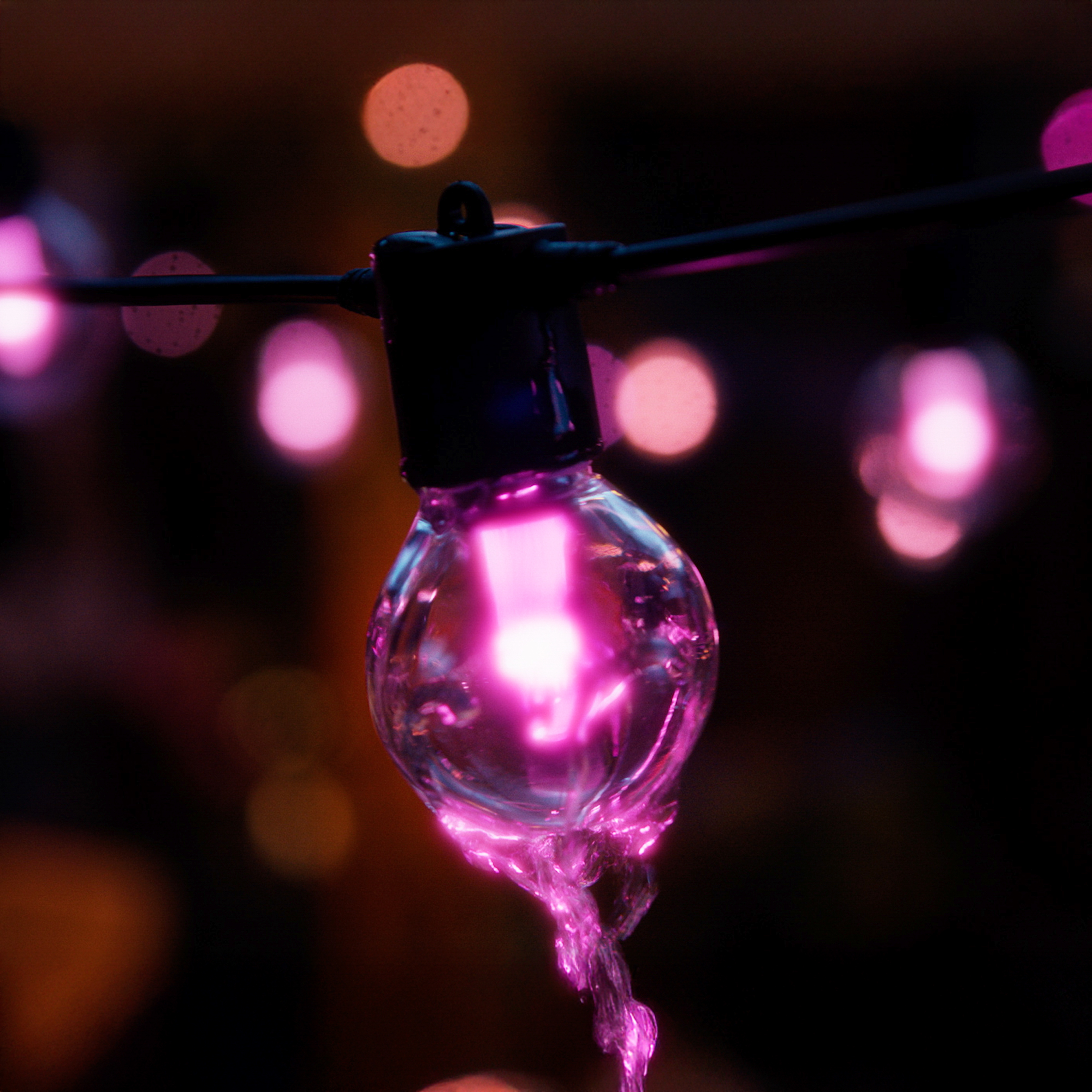 Una lampadina rosa incandescente pende centralmente su uno sfondo scuro con luci bokeh sfocate.