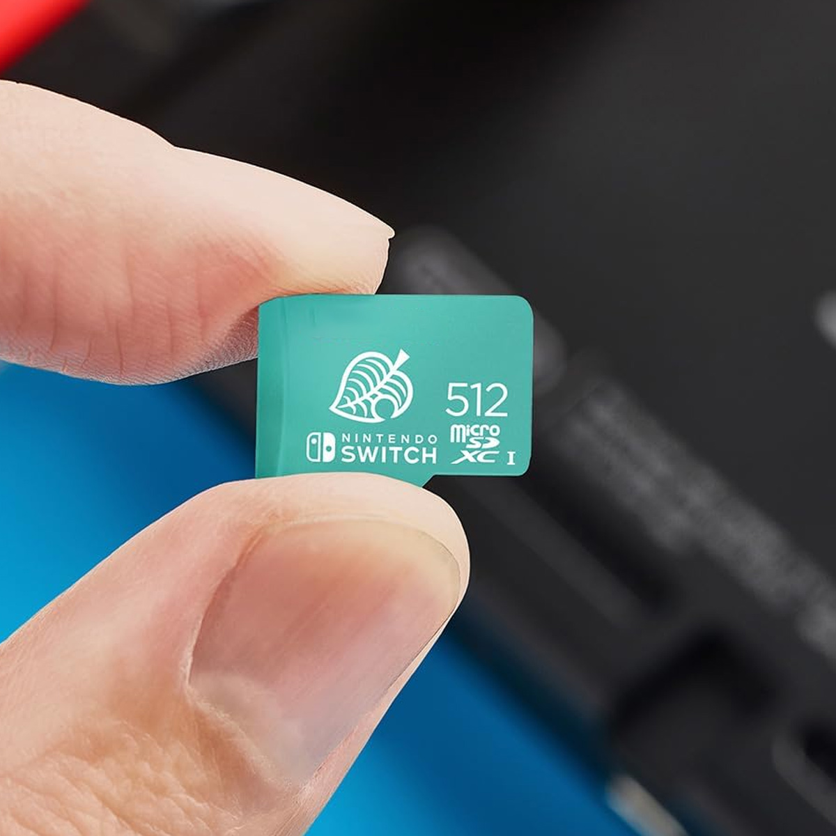 Eine Hand hält eine türkisfarbene 512-GB-Nintendo-Switch-MicroSD-Karte vor dunklem und blauem Hintergrund.