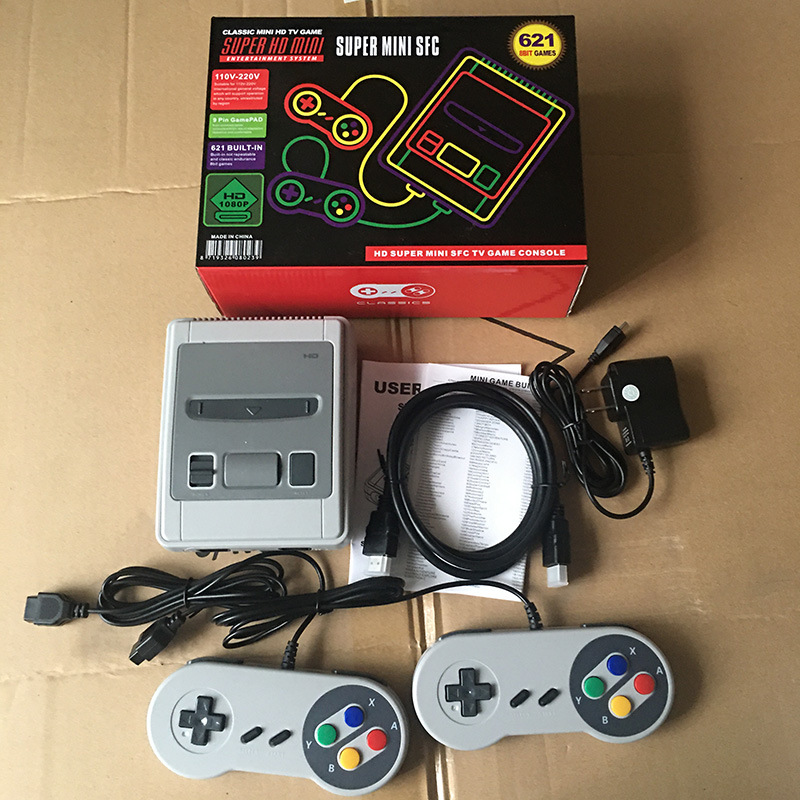 Retro-Spielekonsole mit grauer Hauptkonsole, zwei Controllern, Kabeln, Netzteil und OVP auf Karton.