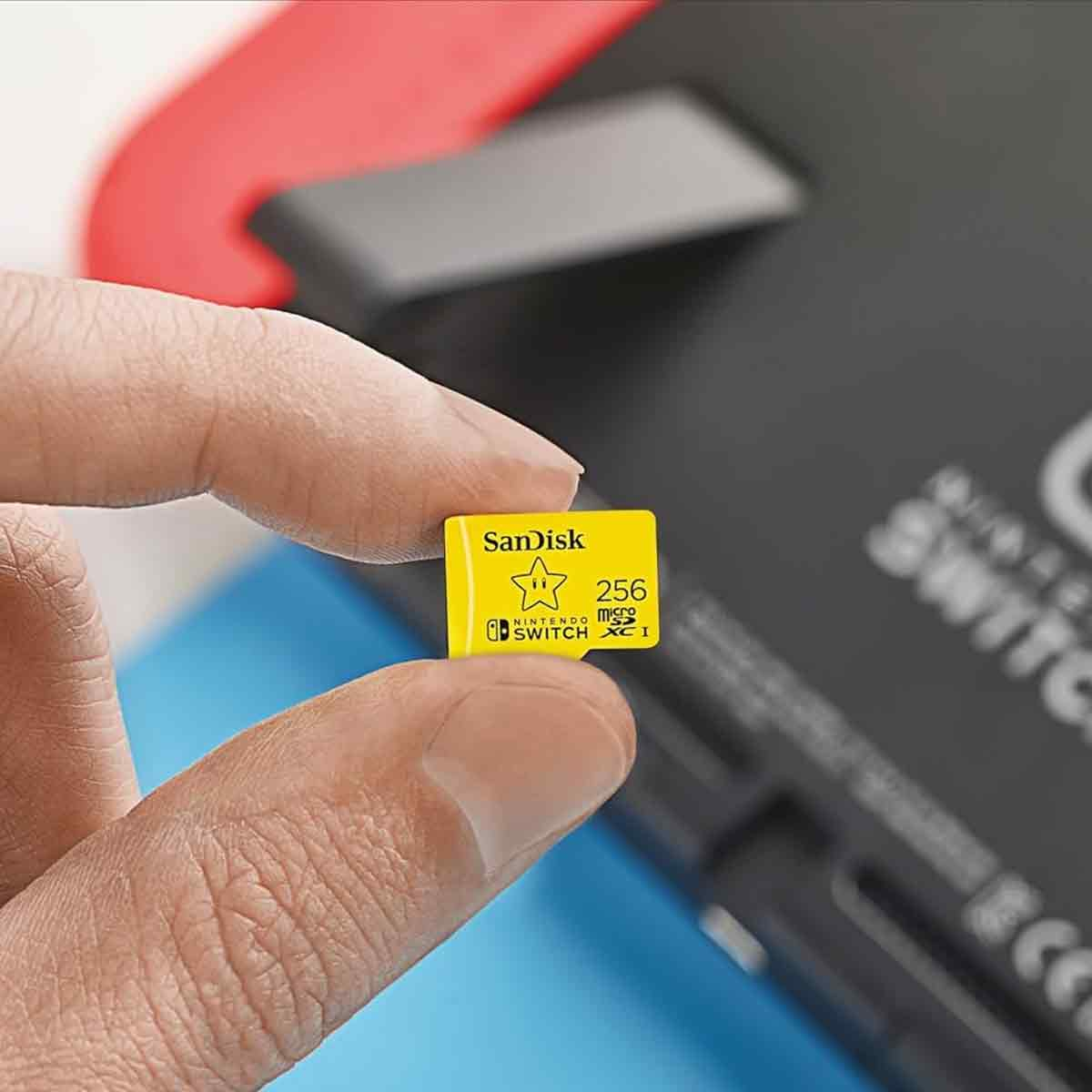 Eine Hand hält eine gelbe SanDisk microSD-Karte vor einer Nintendo Switch Konsole.