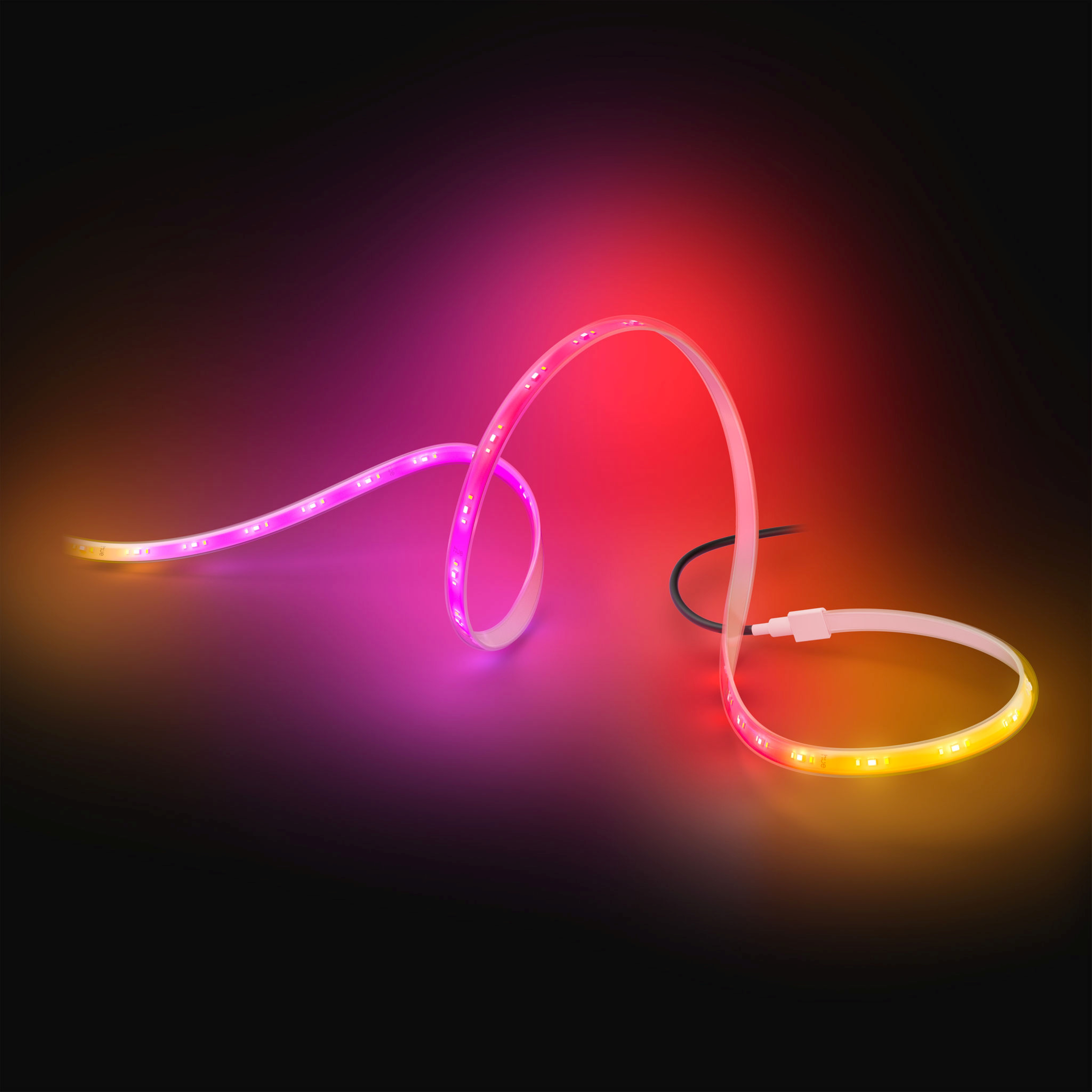 Una striscia LED flessibile si avvolge su uno sfondo scuro, brillando in tonalità vivaci di rosa e arancione.
