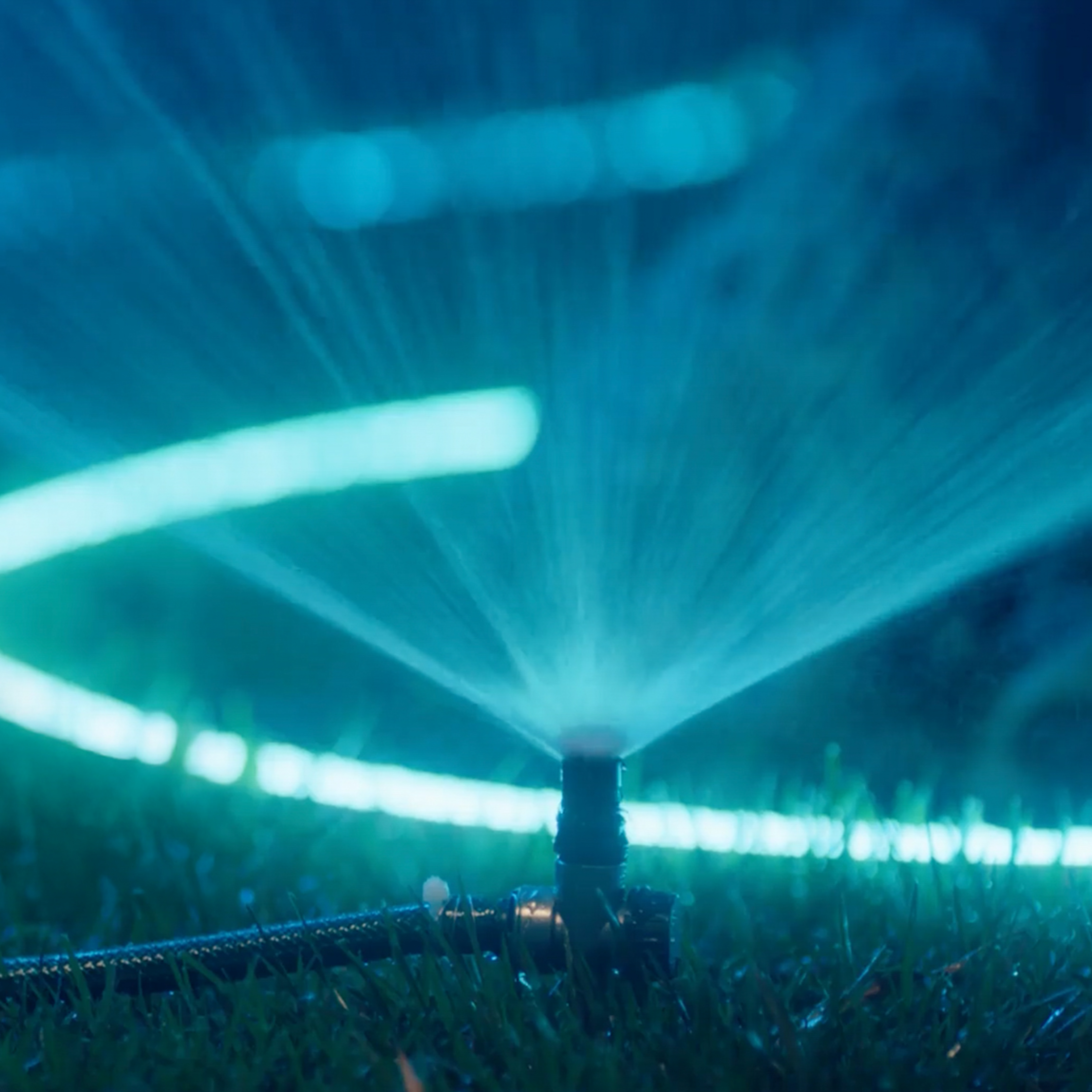Un irrigatore da prato spruzza acqua sull'erba di notte, con una manguera da giardino verde luminoso sullo sfondo.