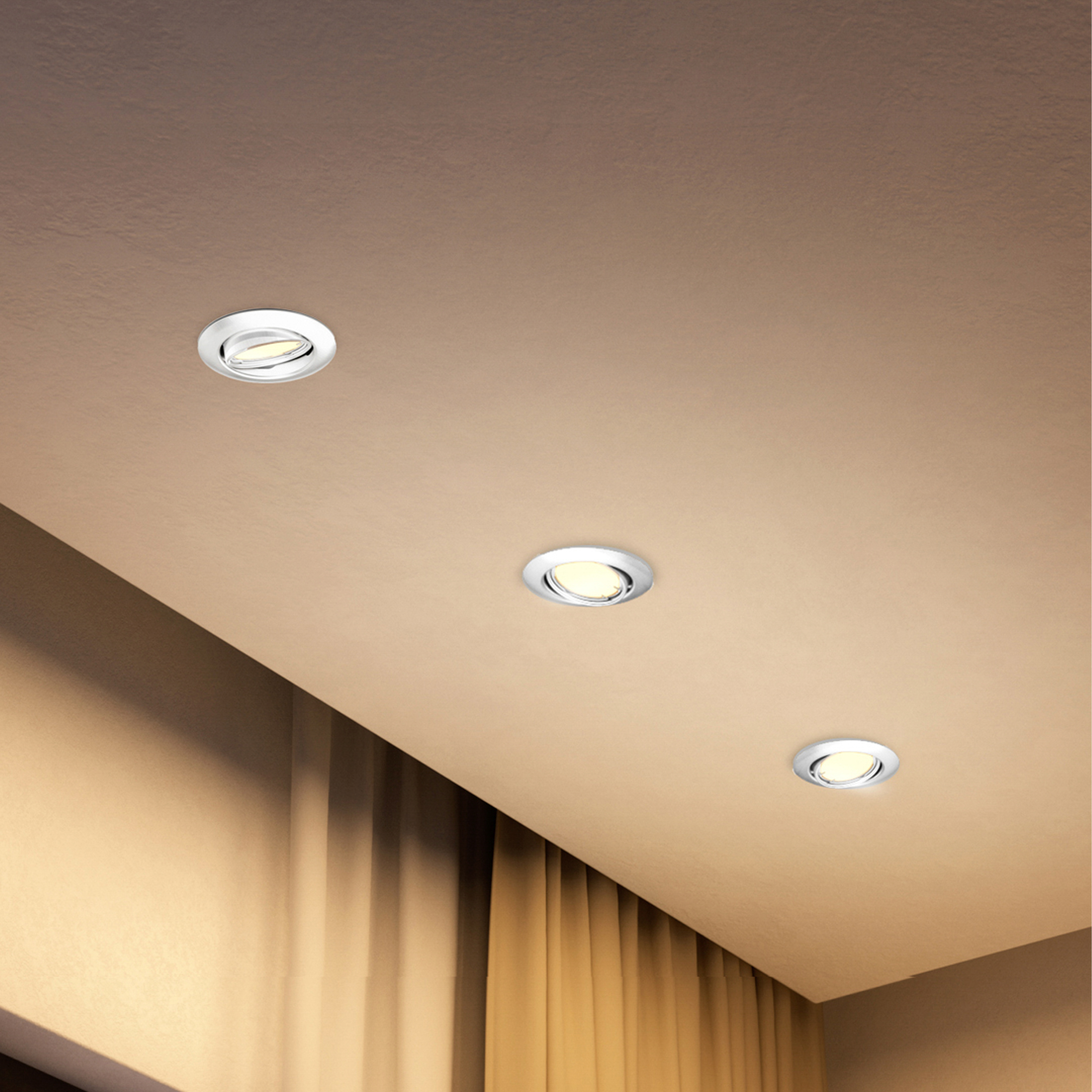 Tre faretti da incasso rotondi bianchi in un soffitto beige sopra tende gialle.