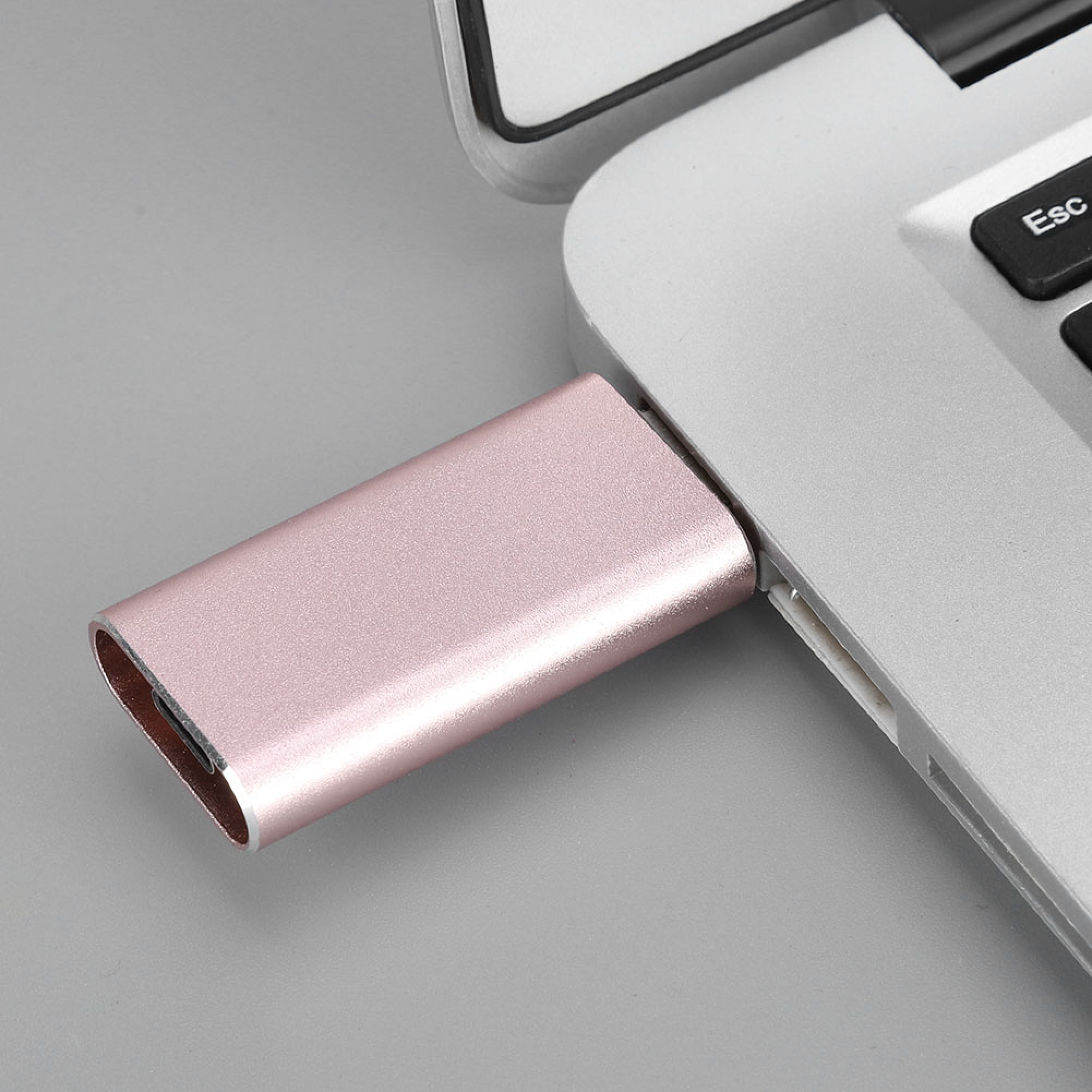Ein rosafarbener USB-C-Adapter steckt im Seitenanschluss eines silbernen Laptops.