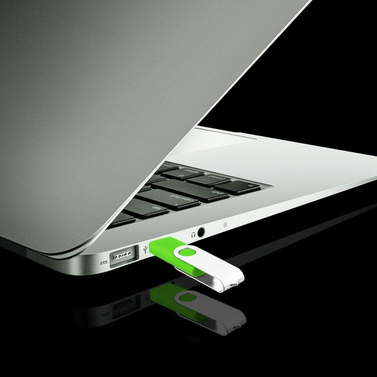 Ein grüner und silberner USB-Stick steckt im seitlichen Anschluss eines offenen silbernen Laptops auf schwarzem Grund.