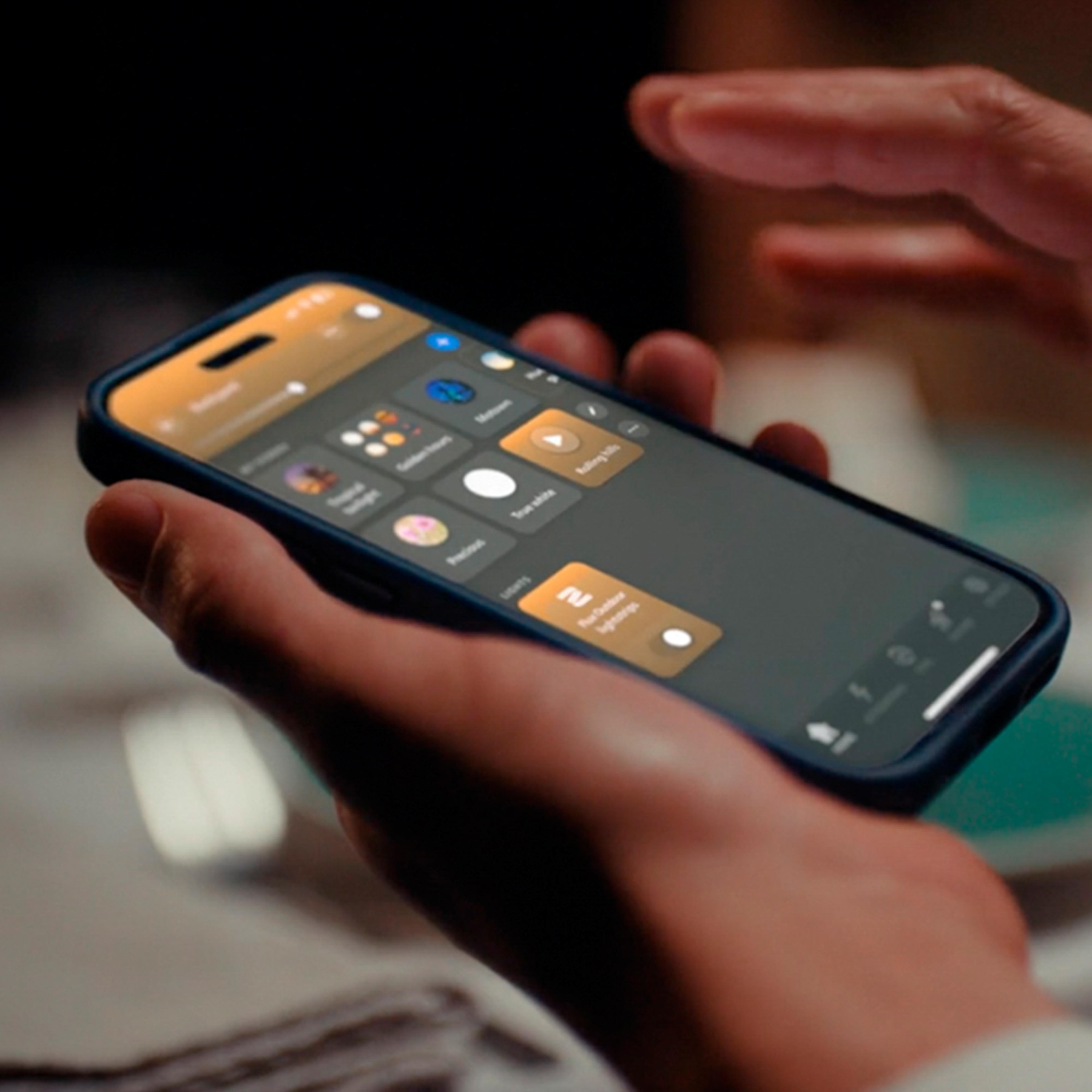 Una persona tiene uno smartphone, usando un'app di illuminazione smart con riquadri arancioni e bianchi.