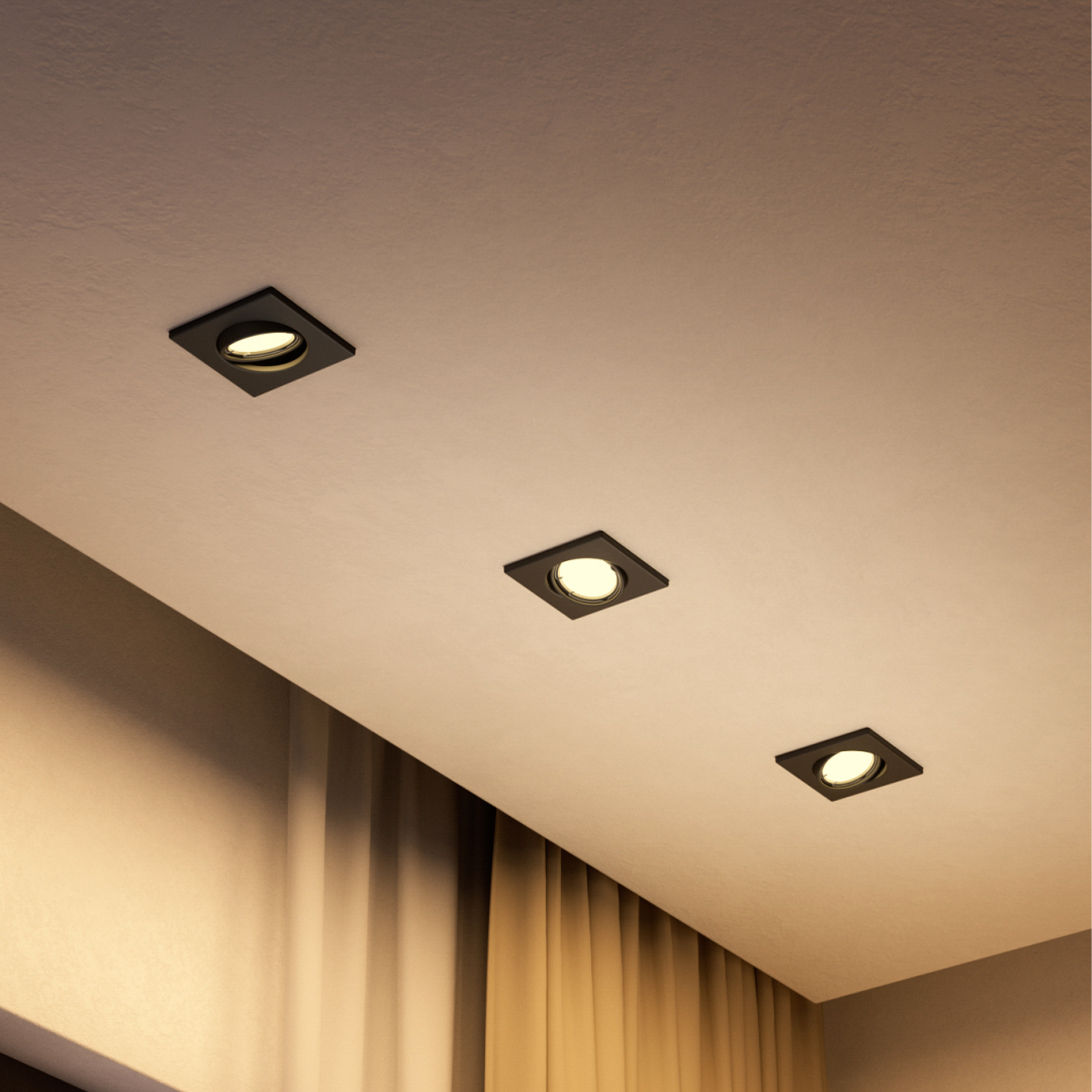 Tre faretti a incasso neri illuminano un soffitto chiaro vicino a tende beige.
