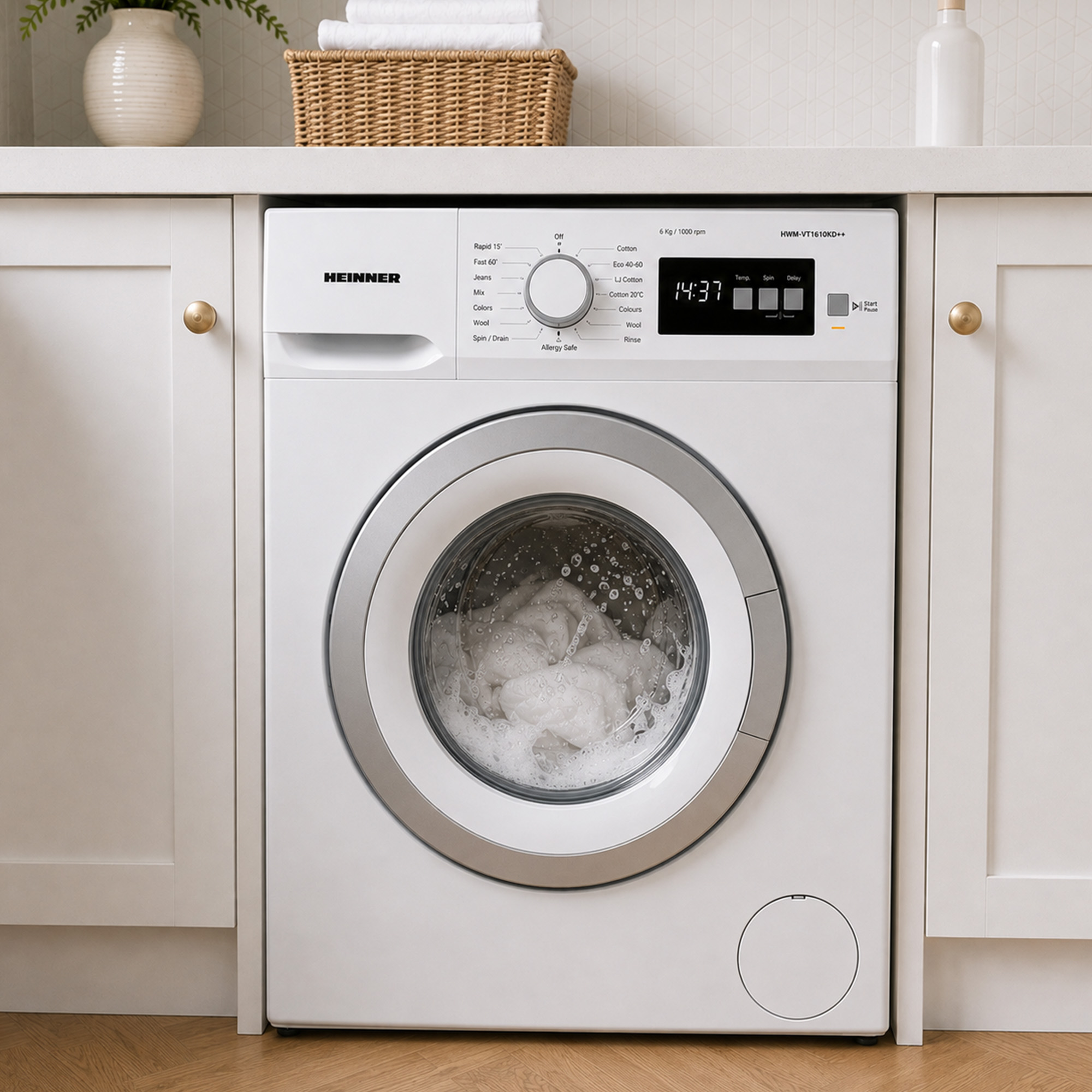 A white Heinner washing machine is built into a white kitchen counter, with clothes visible in the soapy drum.